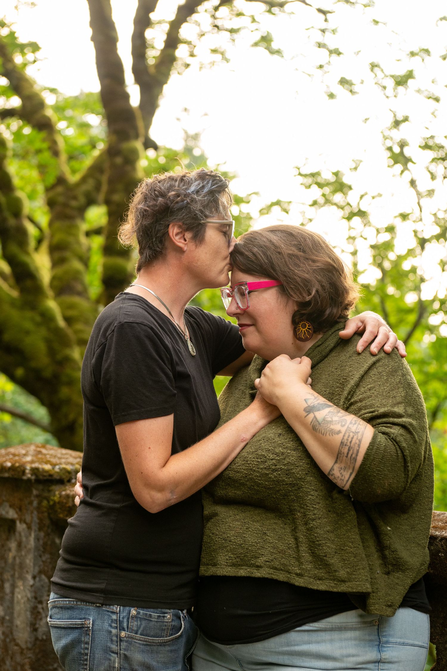 Two people share an intimate embrace while sitting outdoors surrounded by green foliage.