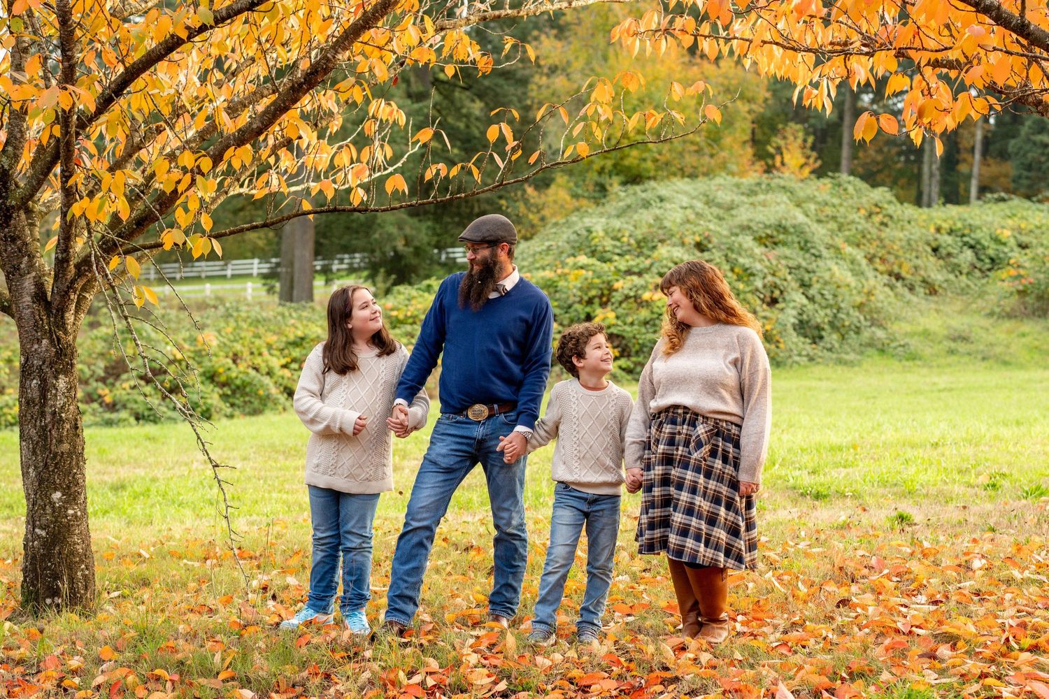 A family enjoying autumn weather beneath golden trees with fallen leaves scattered around.