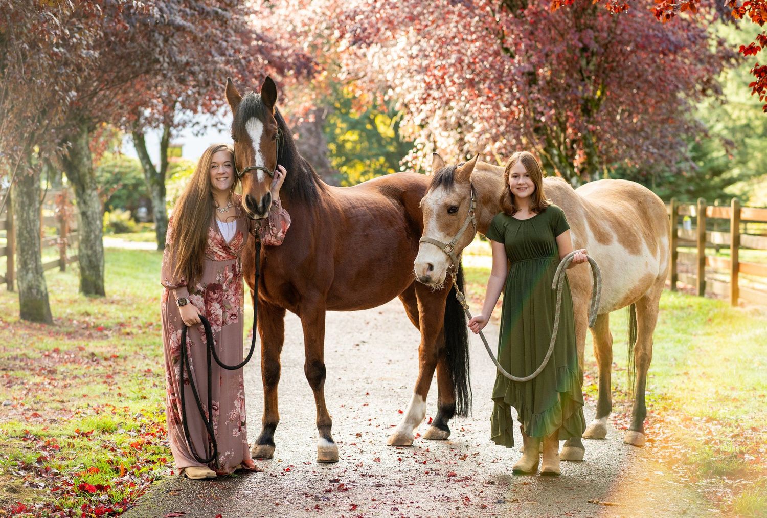 Two majestic horses stand with their handlers in a vibrant autumn forest setting with red and orange foliage.