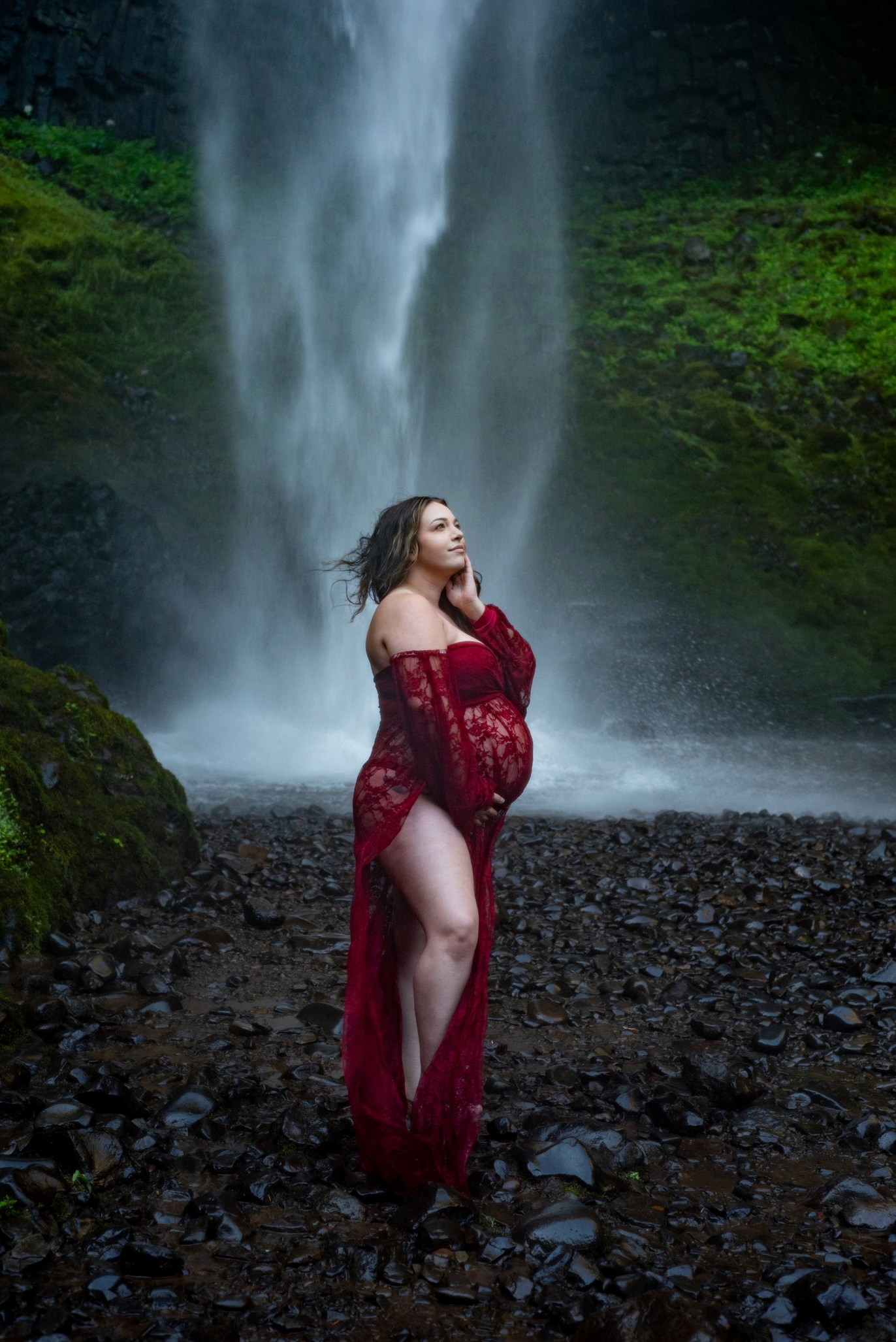 Woman in red dress poses dramatically in front of majestic waterfall.
