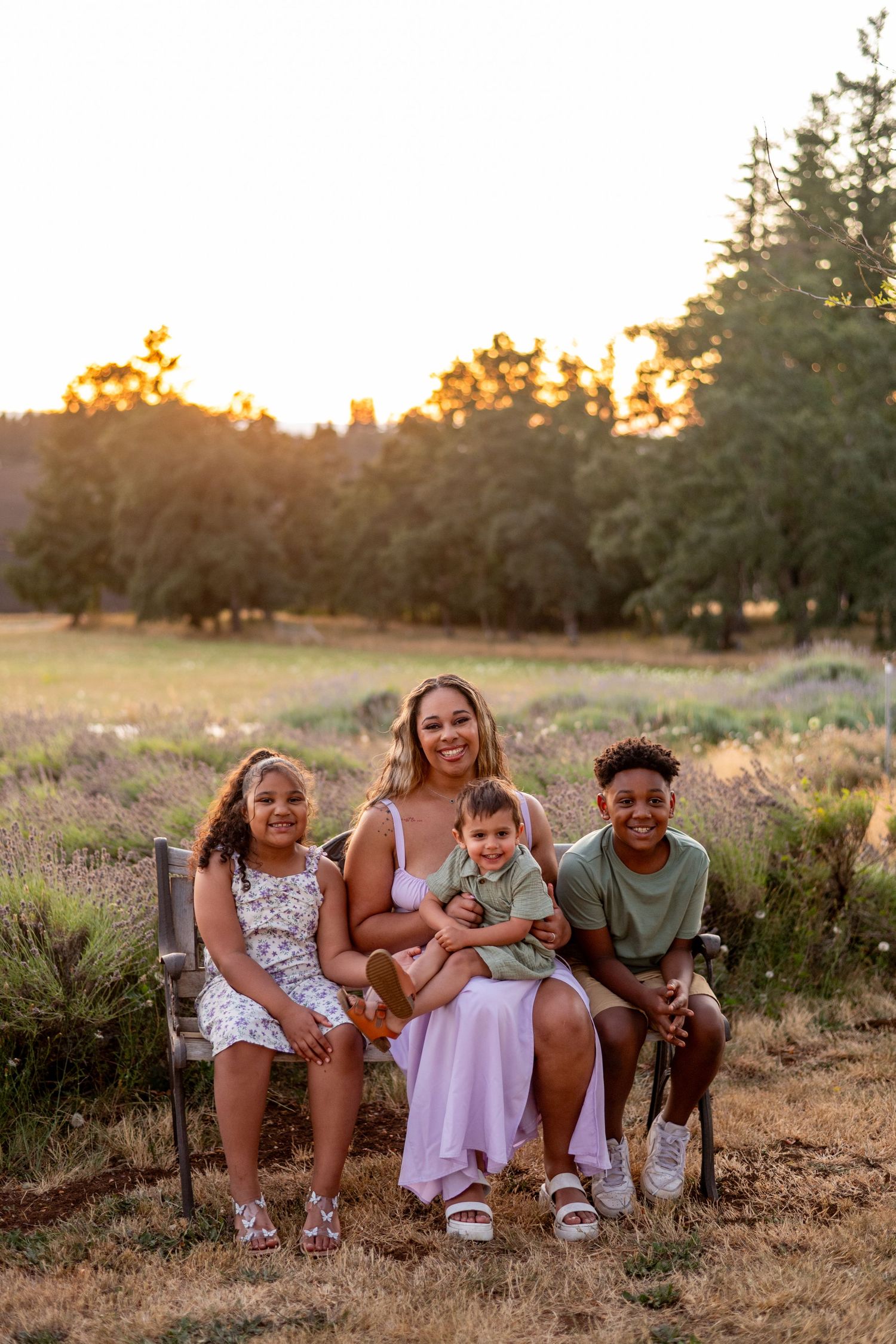 Group of people sitting together laughing and having fun in a grassy field at golden hour sunset.
