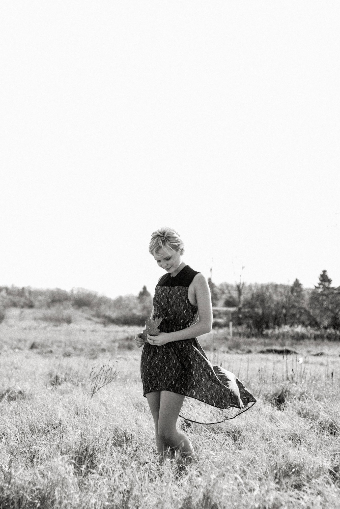 Dreamy monochrome series of someone in a patterned dress walking through a sunlit meadow.
