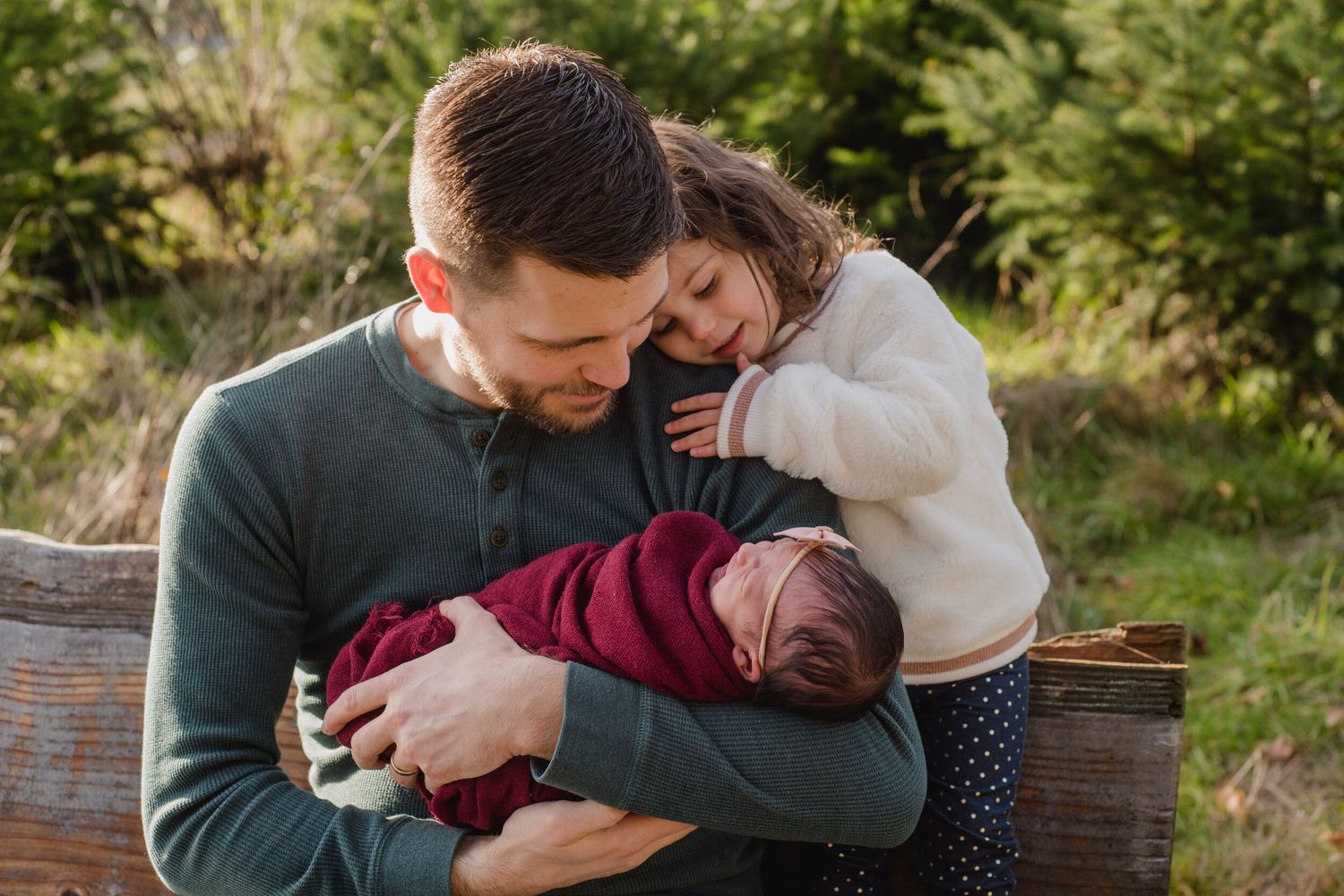A tender family moment shared on a wooden bench in a natural setting.
