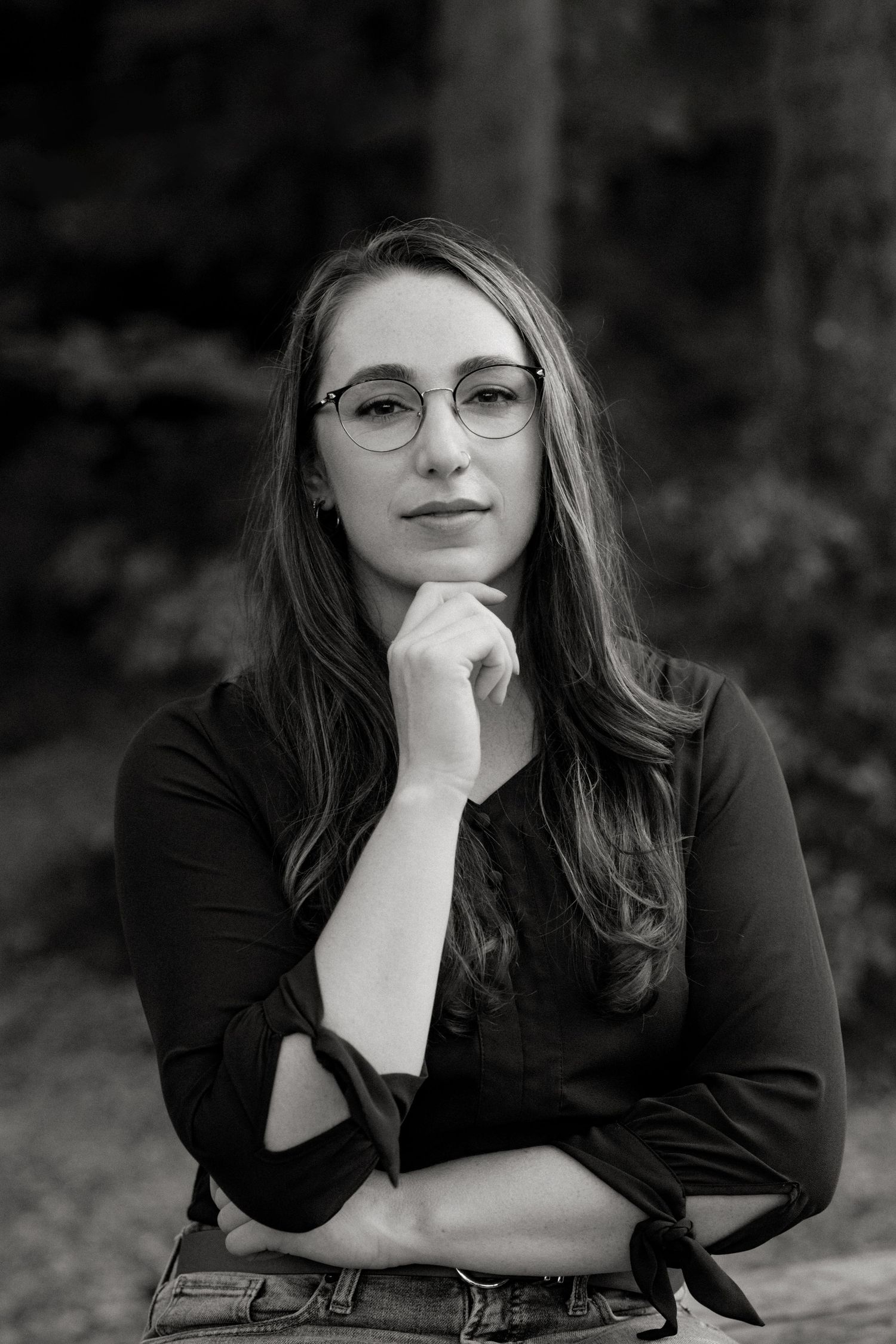 Artistic monochrome portrait of someone in glasses and dark clothing resting their chin on their hand.