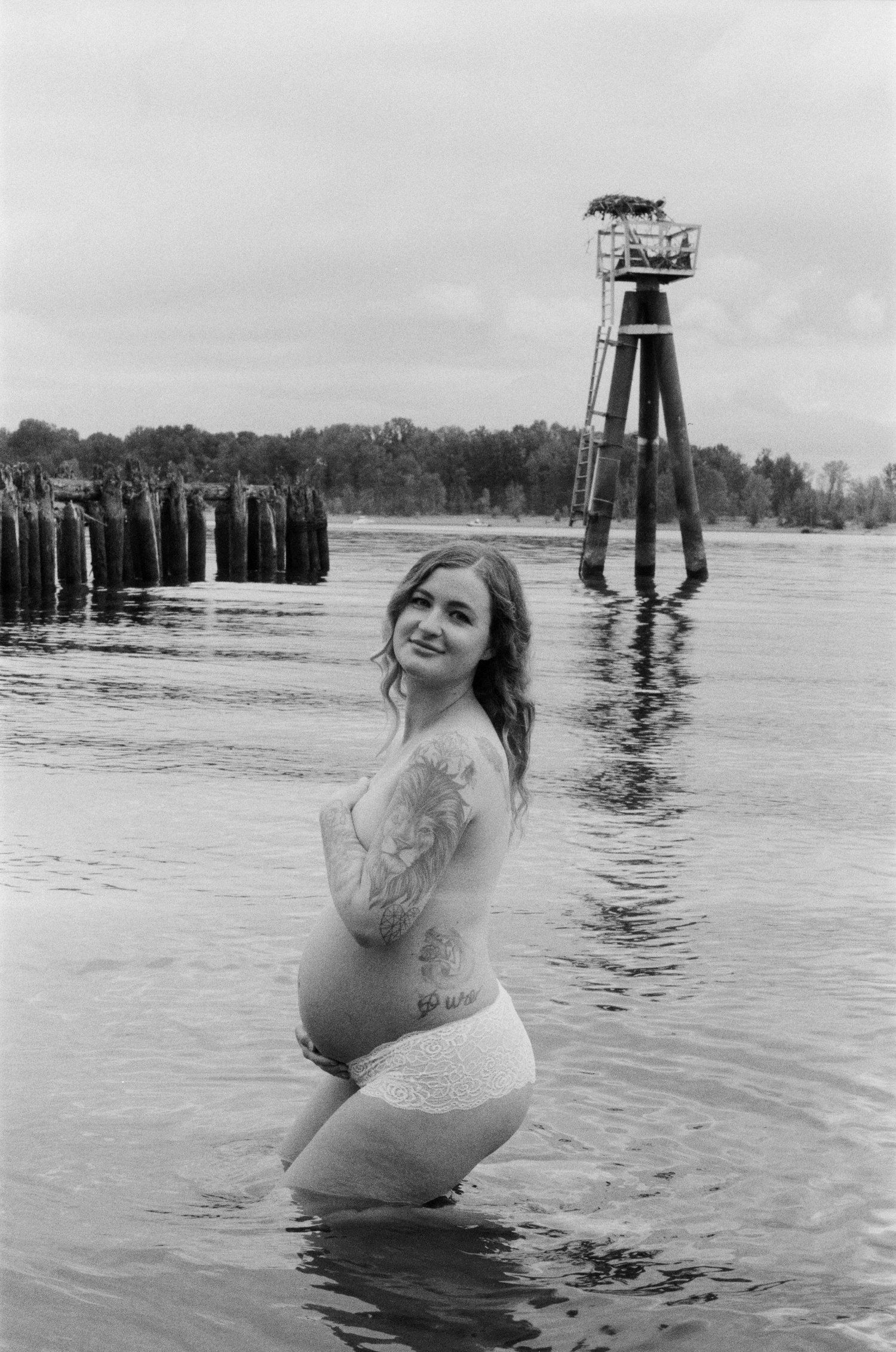 A figure in white poses in water with a vintage industrial structure visible in the background.