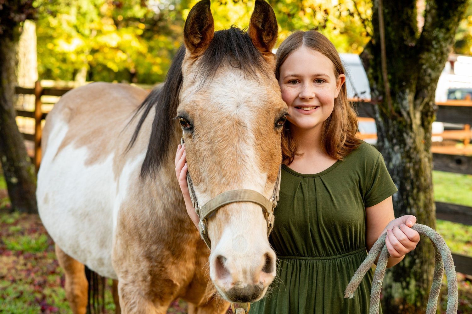 A paint horse and young person pose together on an autumn day.