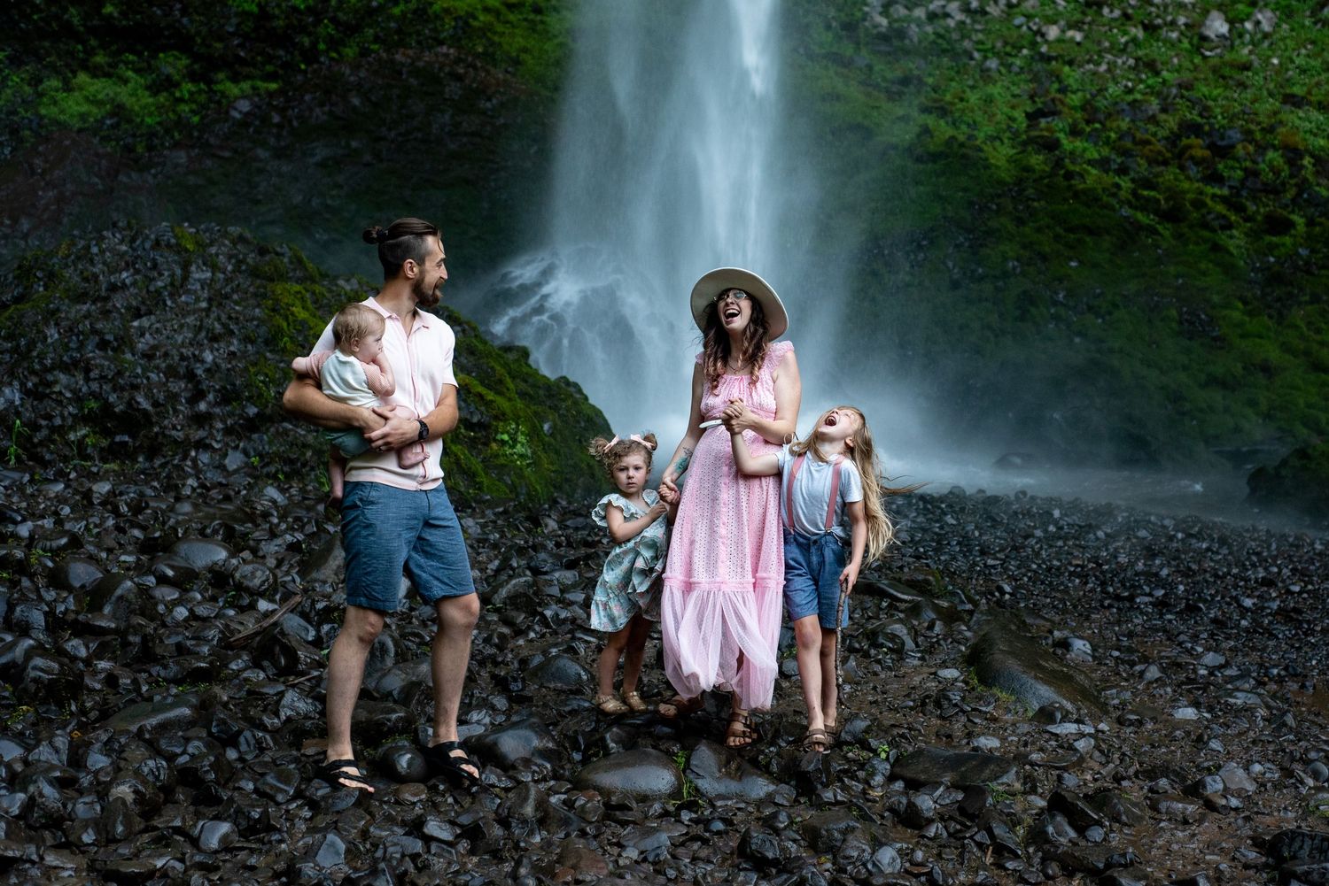 A family group stands on rocky terrain beneath a towering waterfall.