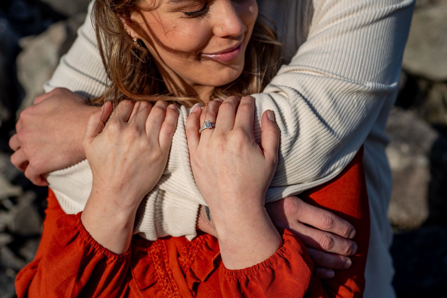 Close-up view of intertwined hands with someone wearing a red dress and cream colored sweater in warm evening sunlight.