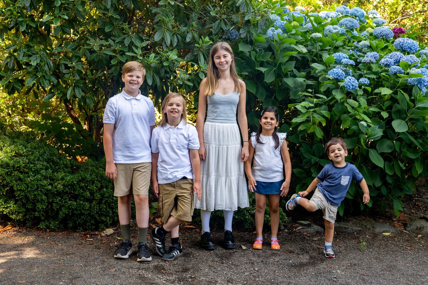 A group standing in a garden path with lush green foliage and natural lighting in outdoor family photo session.