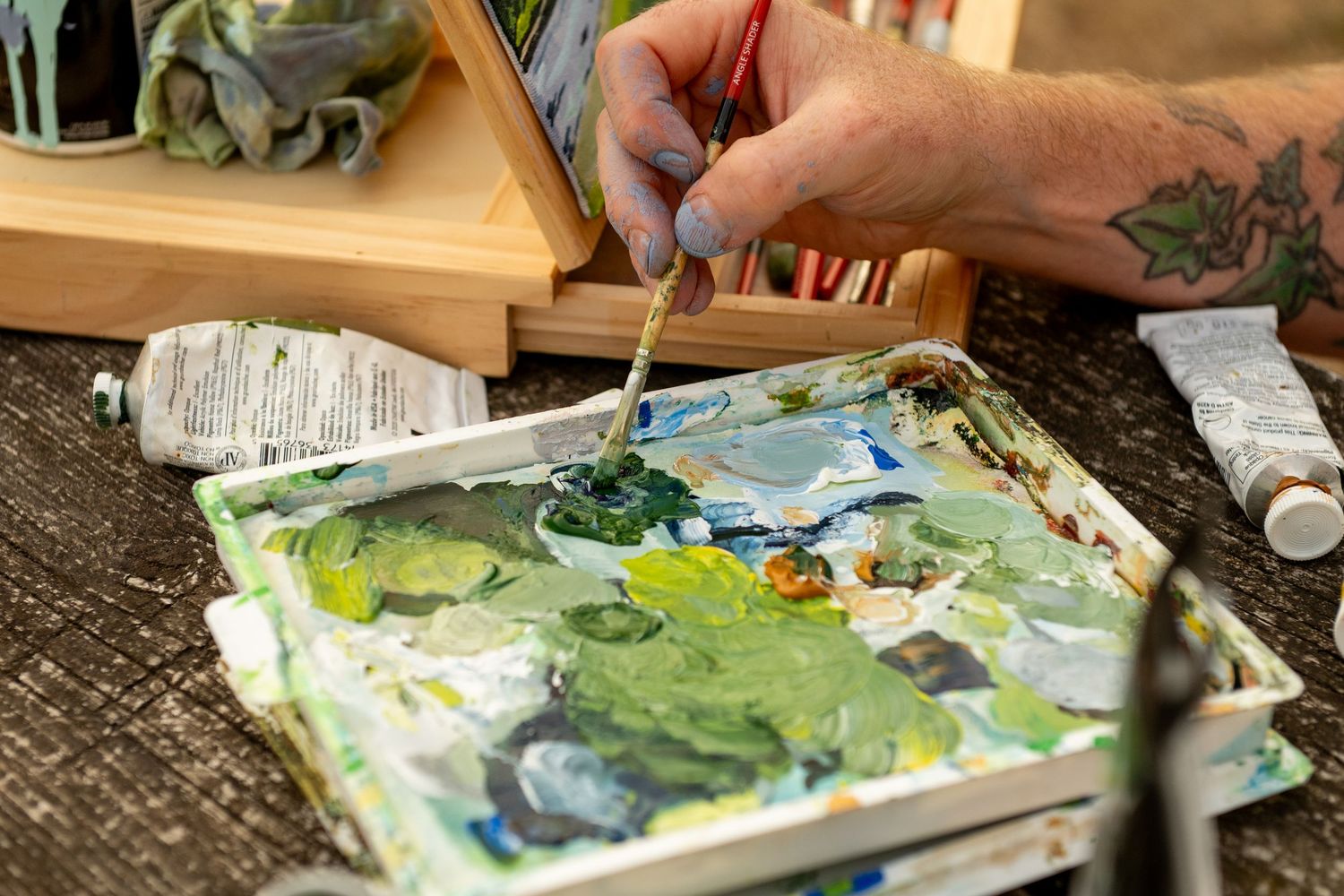 Close-up of art materials including paint brushes and palette with green paint being mixed on white surface.