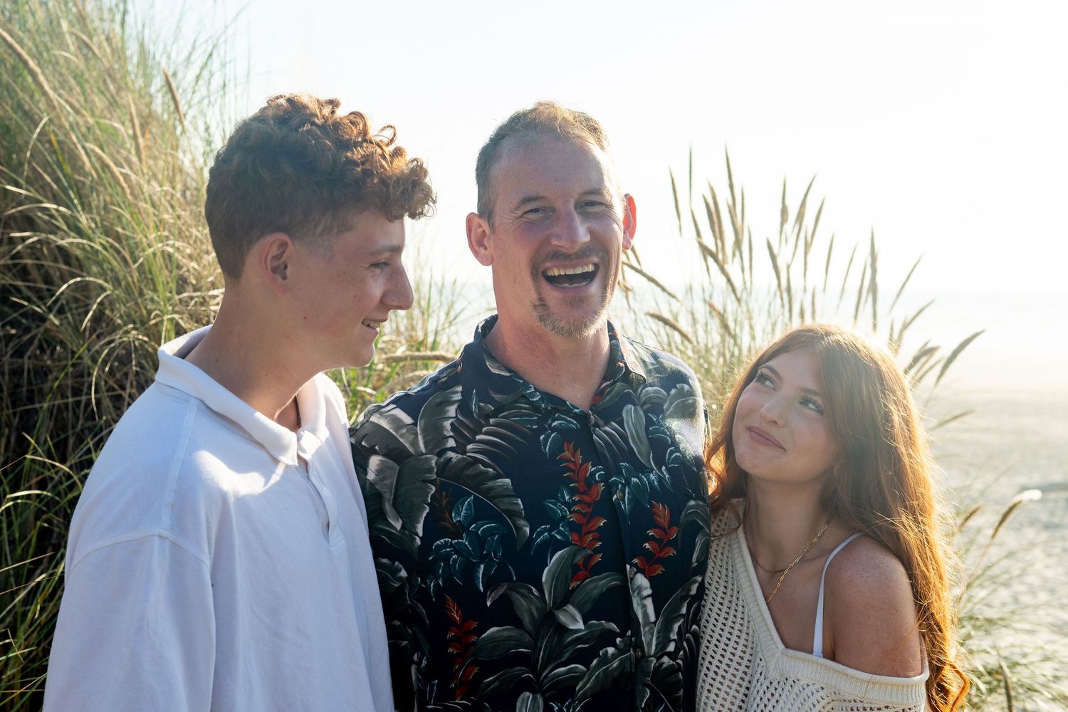 Young people laughing and embracing at sunset in tall grass near beach.