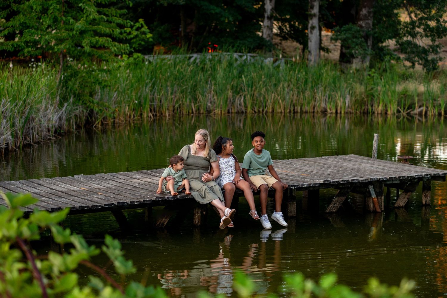 People walking and lounging on small wooden footbridges across a serene pond surrounded by lush green vegetation.