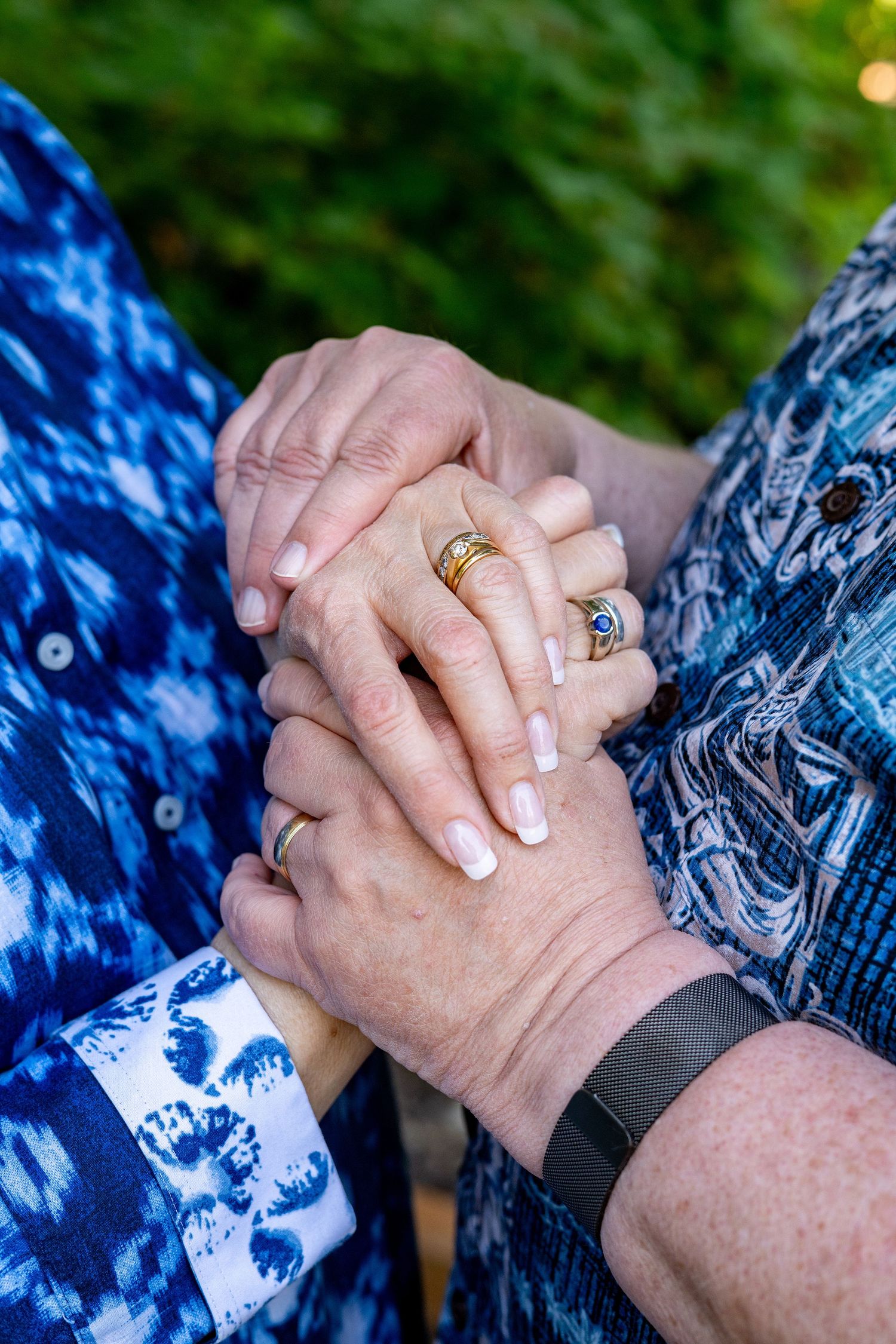 Close-up of clasped hands wearing gold rings and matching blue patterned clothing with a fitness tracker visible.