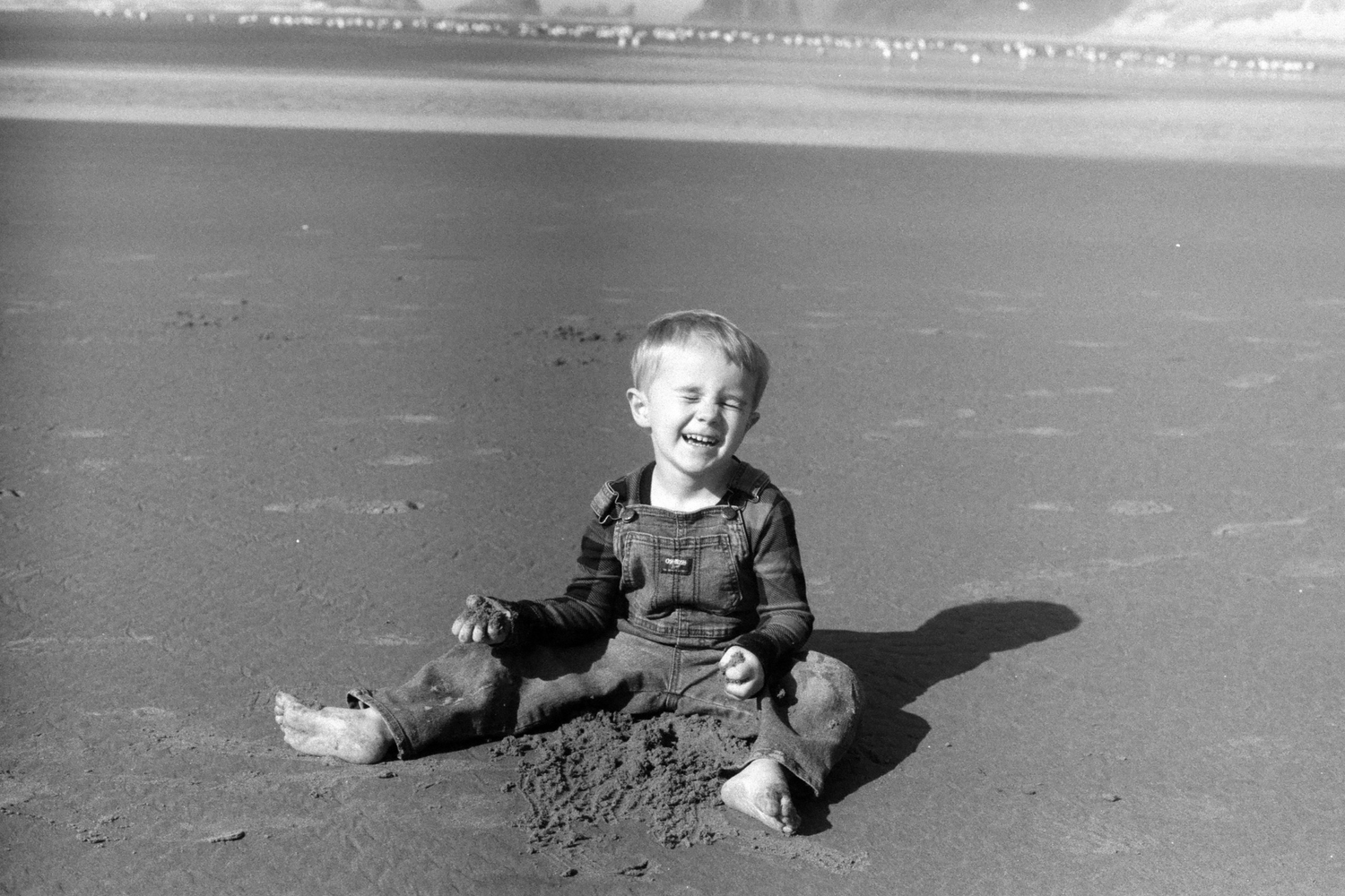 Vintage black and white photo of child playing in sand at beach.