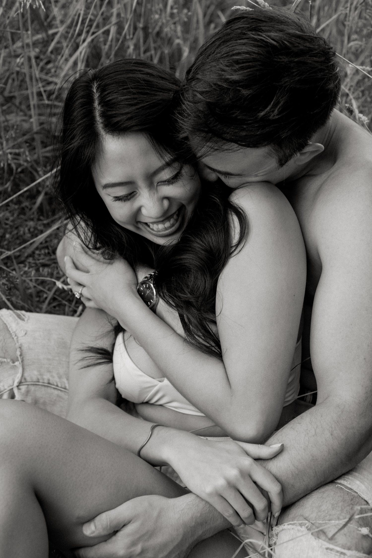 An intimate black and white portrait of a couple embracing in tall grass.