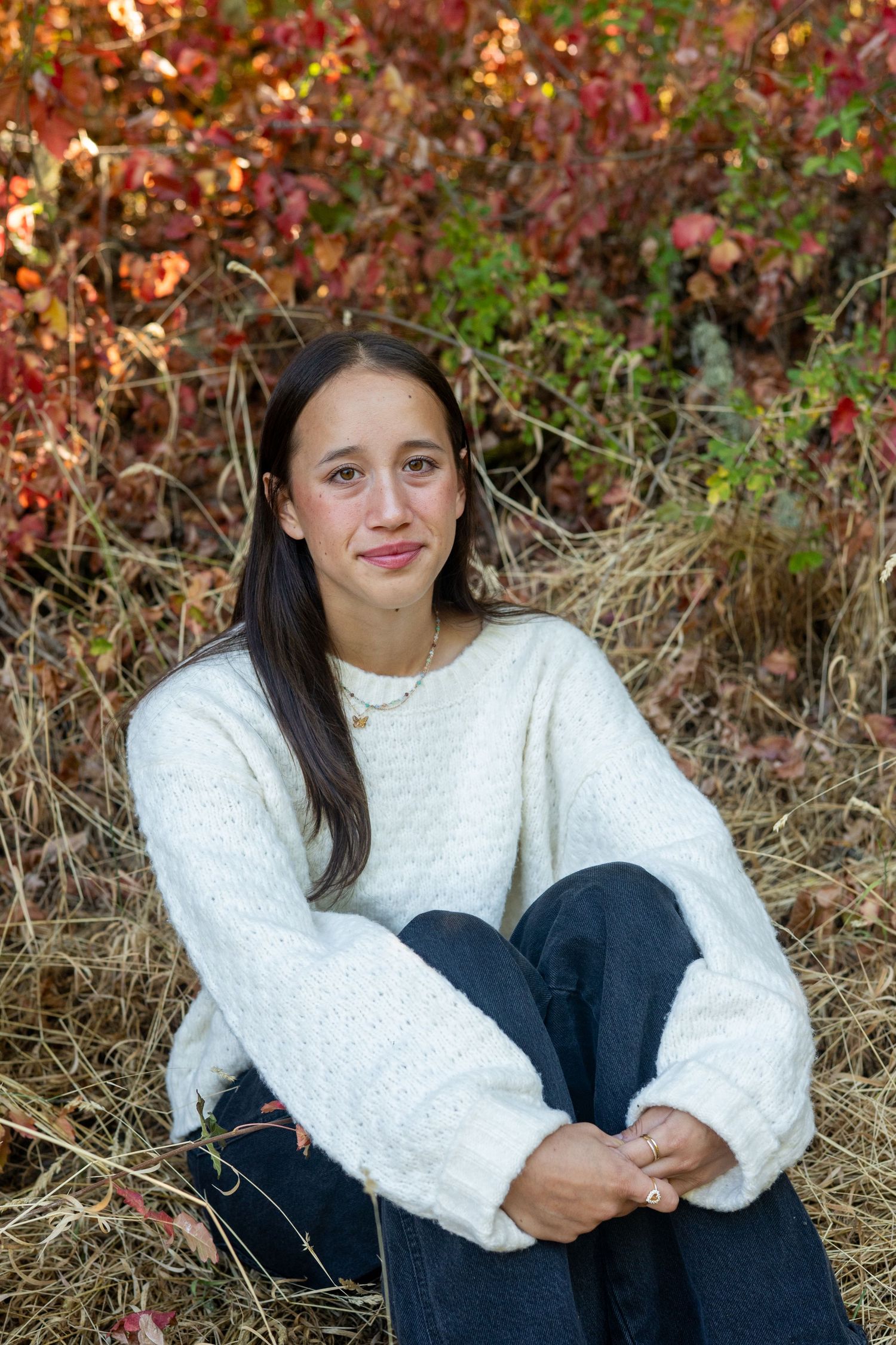 A candid photo series of someone in a cozy white sweater sitting against colorful autumn foliage.