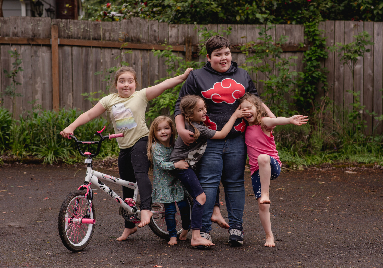 Group posing playfully outdoors with bicycle and fence in background.