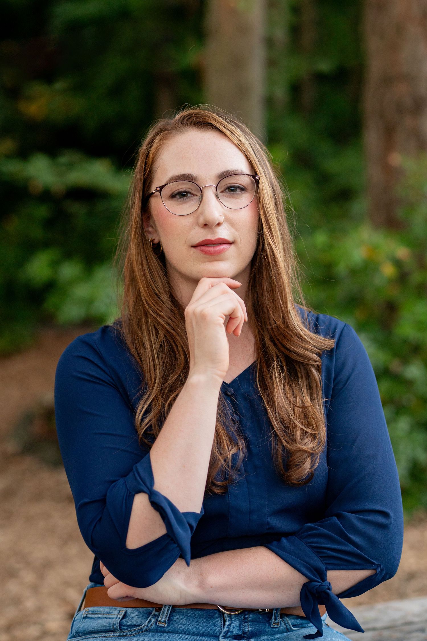 Portrait of someone wearing glasses and a navy blue top posing thoughtfully outdoors with a natural background.
