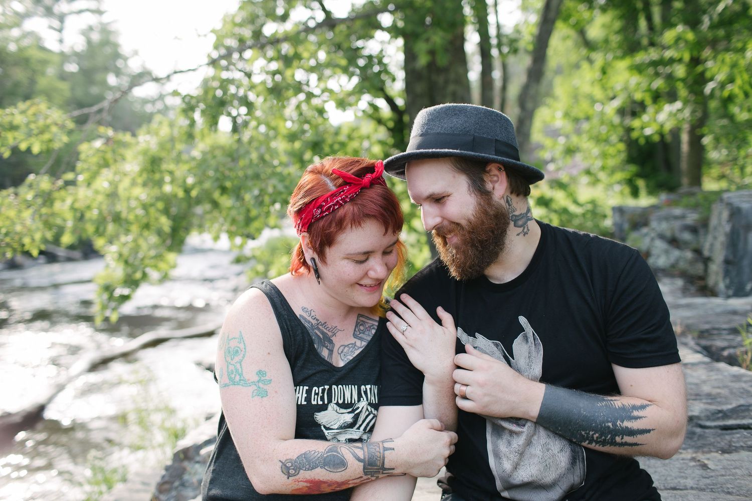 A romantic couple sits together on rocky terrain surrounded by lush greenery in a natural outdoor setting.