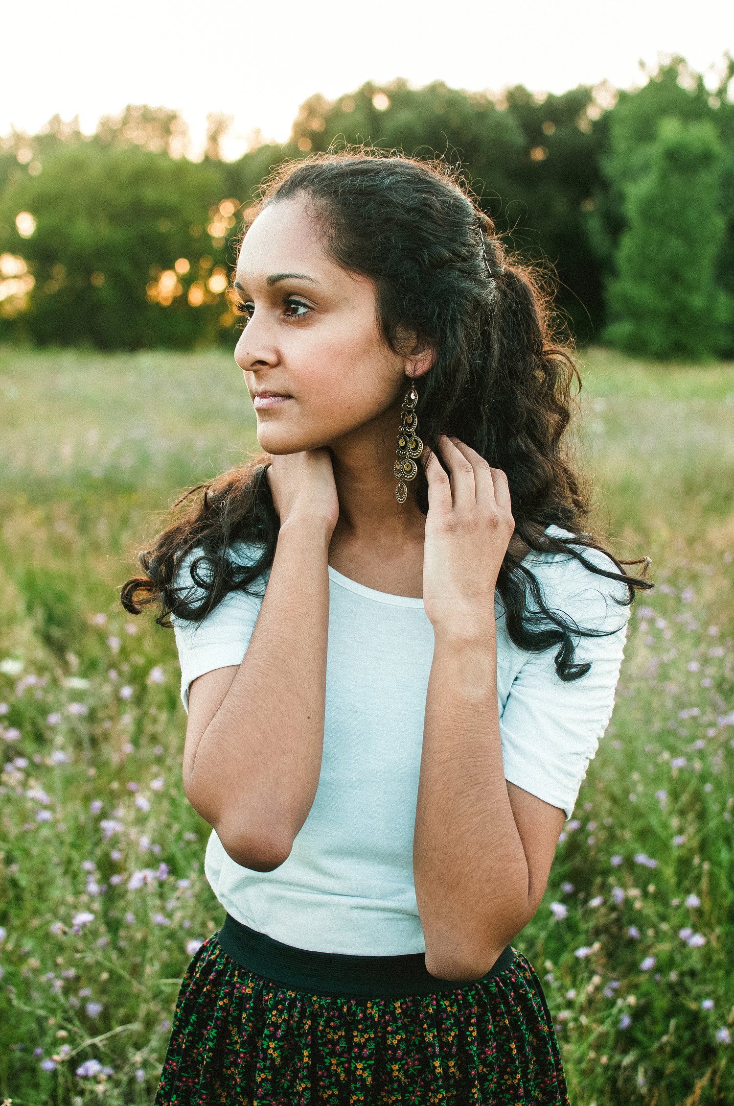 A portrait in a wildflower field at sunset featuring a white top and flowing hair with dangling earrings.