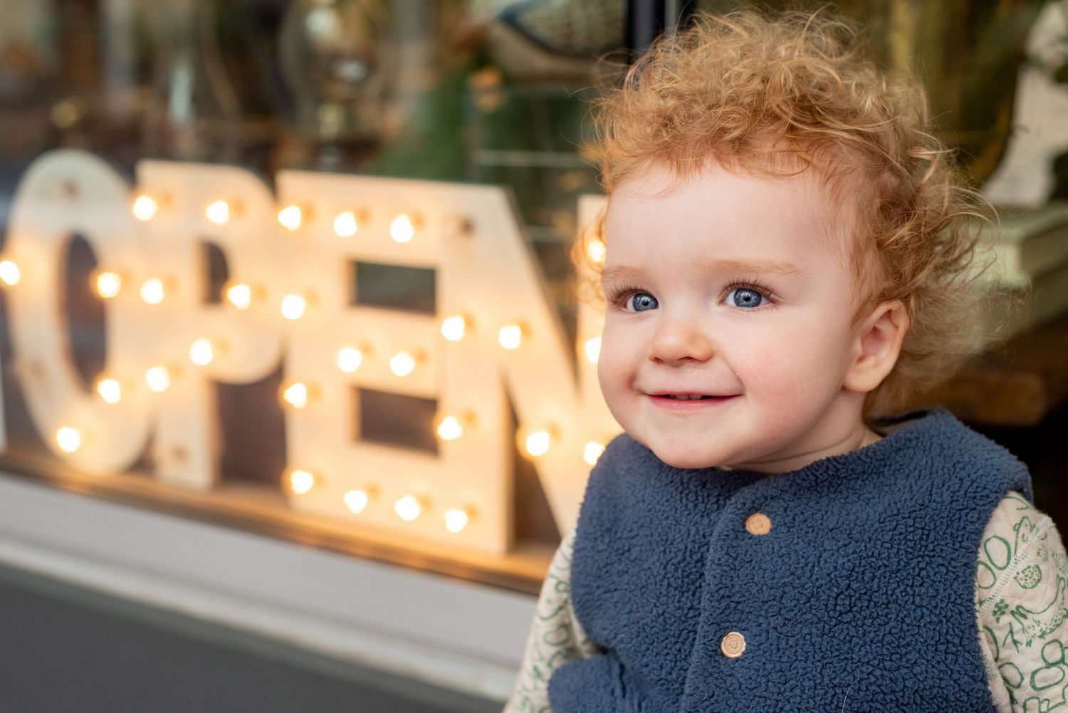 Child wearing navy blue sweater smiles while surrounded by glowing lights in indoor setting.