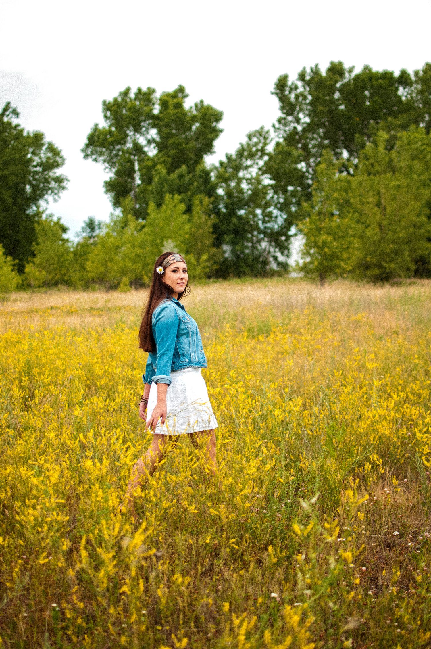 A person in a denim jacket stands in a field of yellow wildflowers on a sunny day.