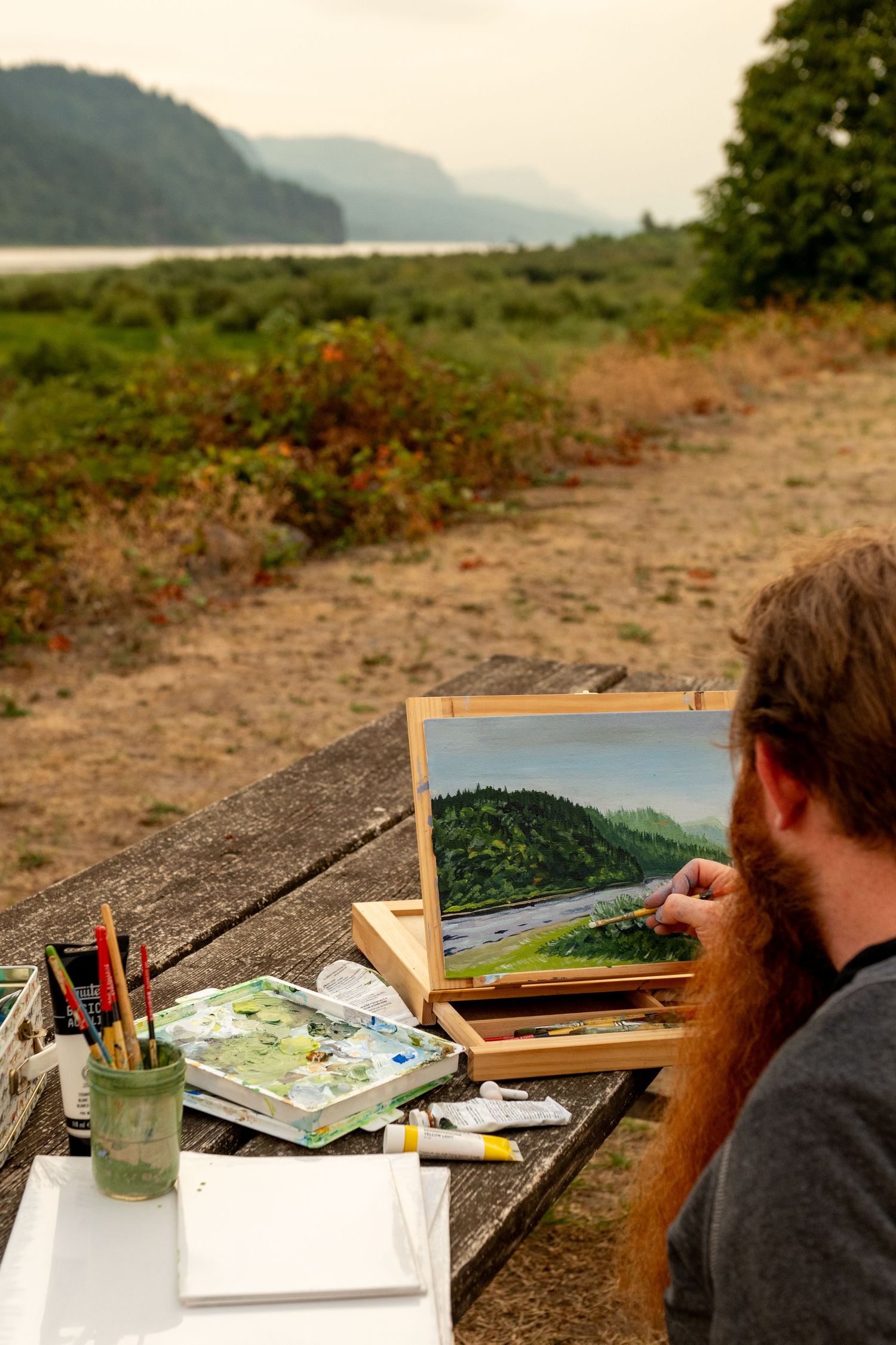 A series of photographs showing an artist painting a landscape on an easel outdoors with mountains in the background.