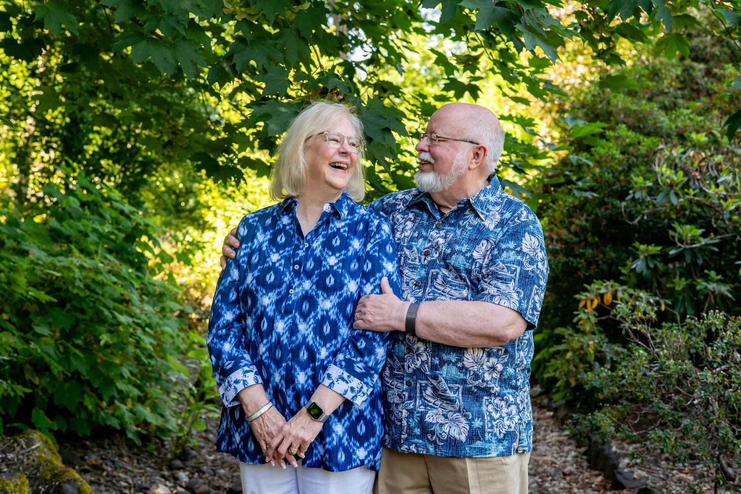 A couple wearing matching blue floral shirts shares a candid moment together outdoors in a garden setting.