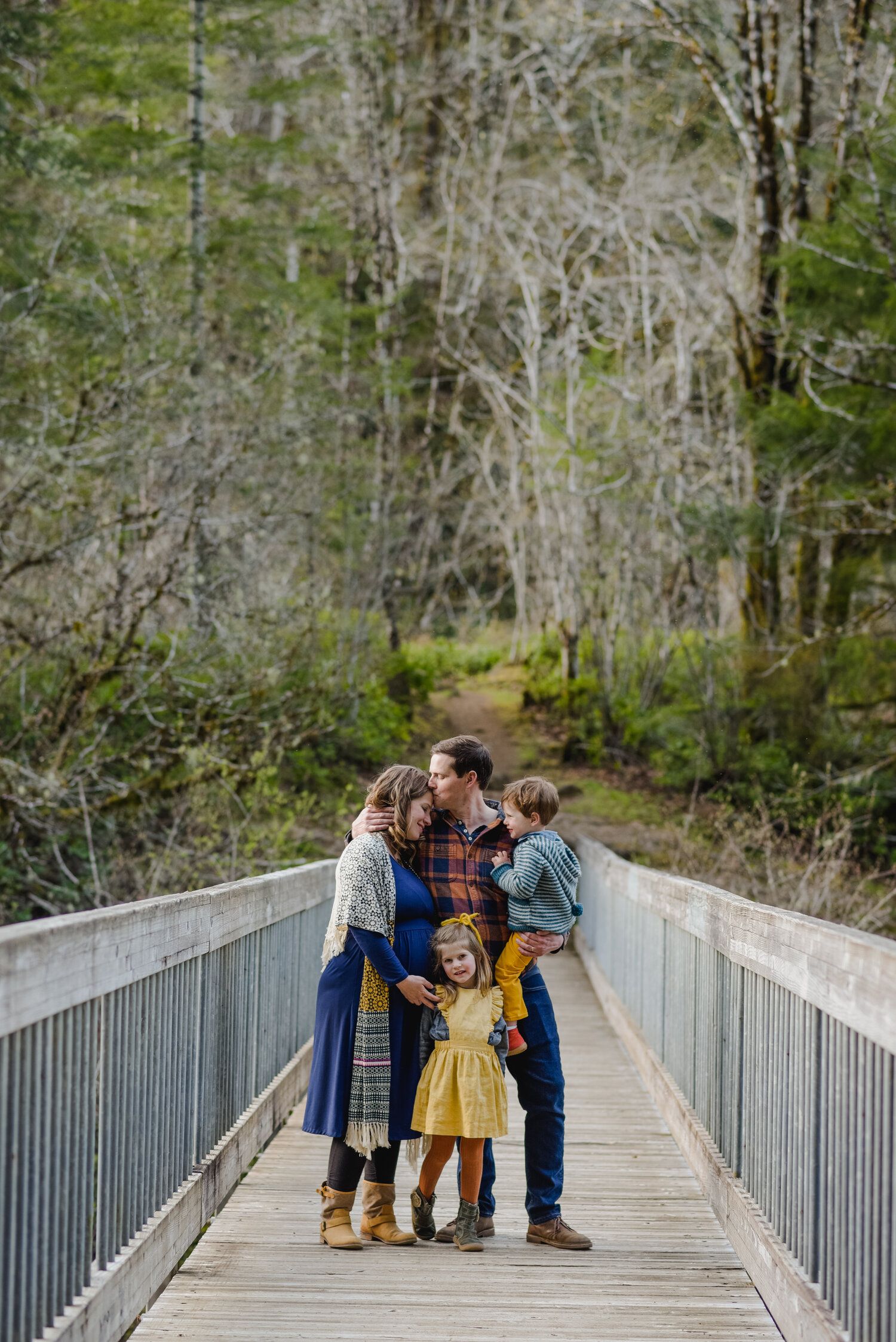 A sweet family moment shared on a wooden footbridge in a misty forest setting.