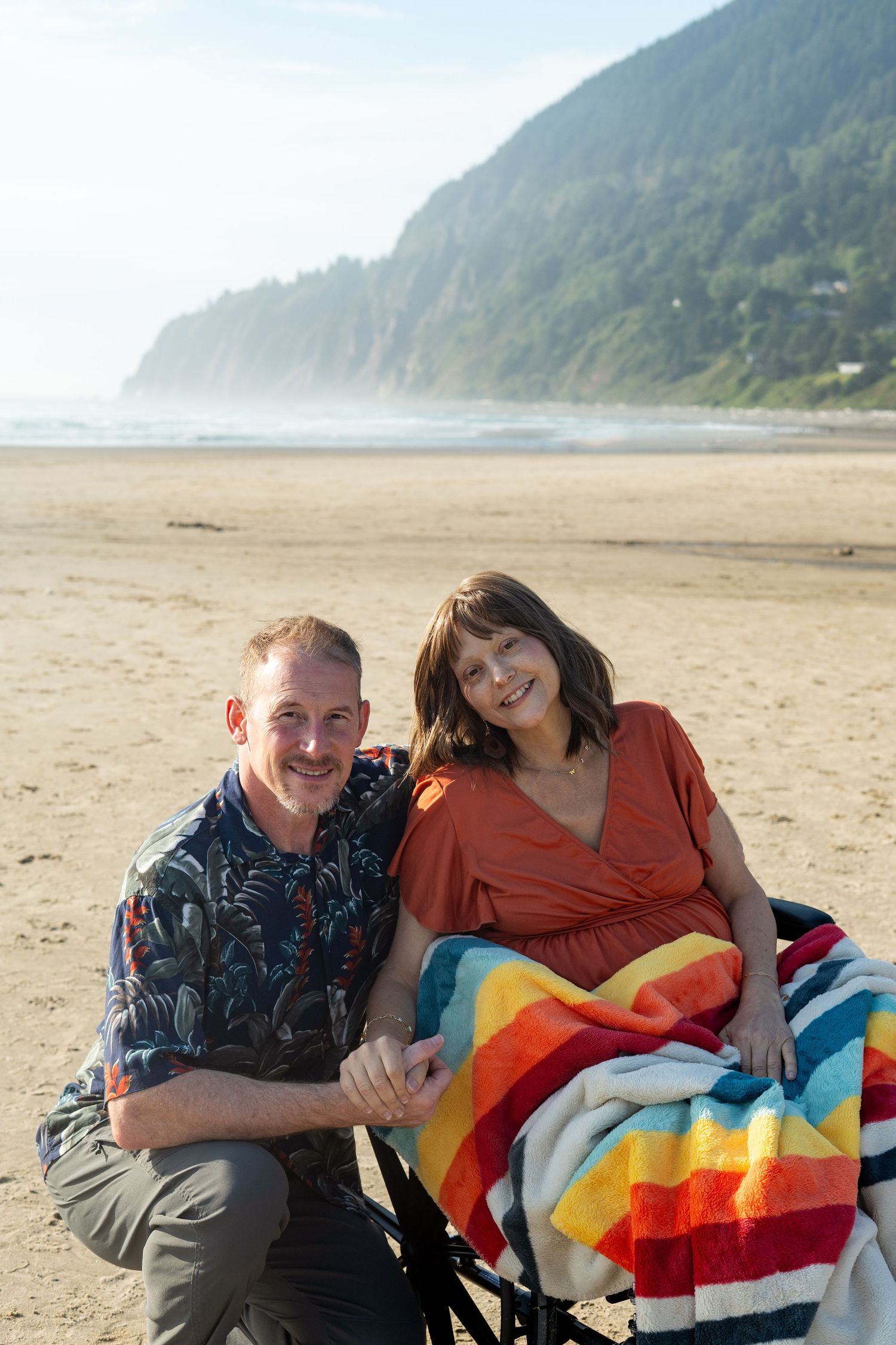 Two people relax with a colorful striped blanket on a foggy Pacific Northwest beach.