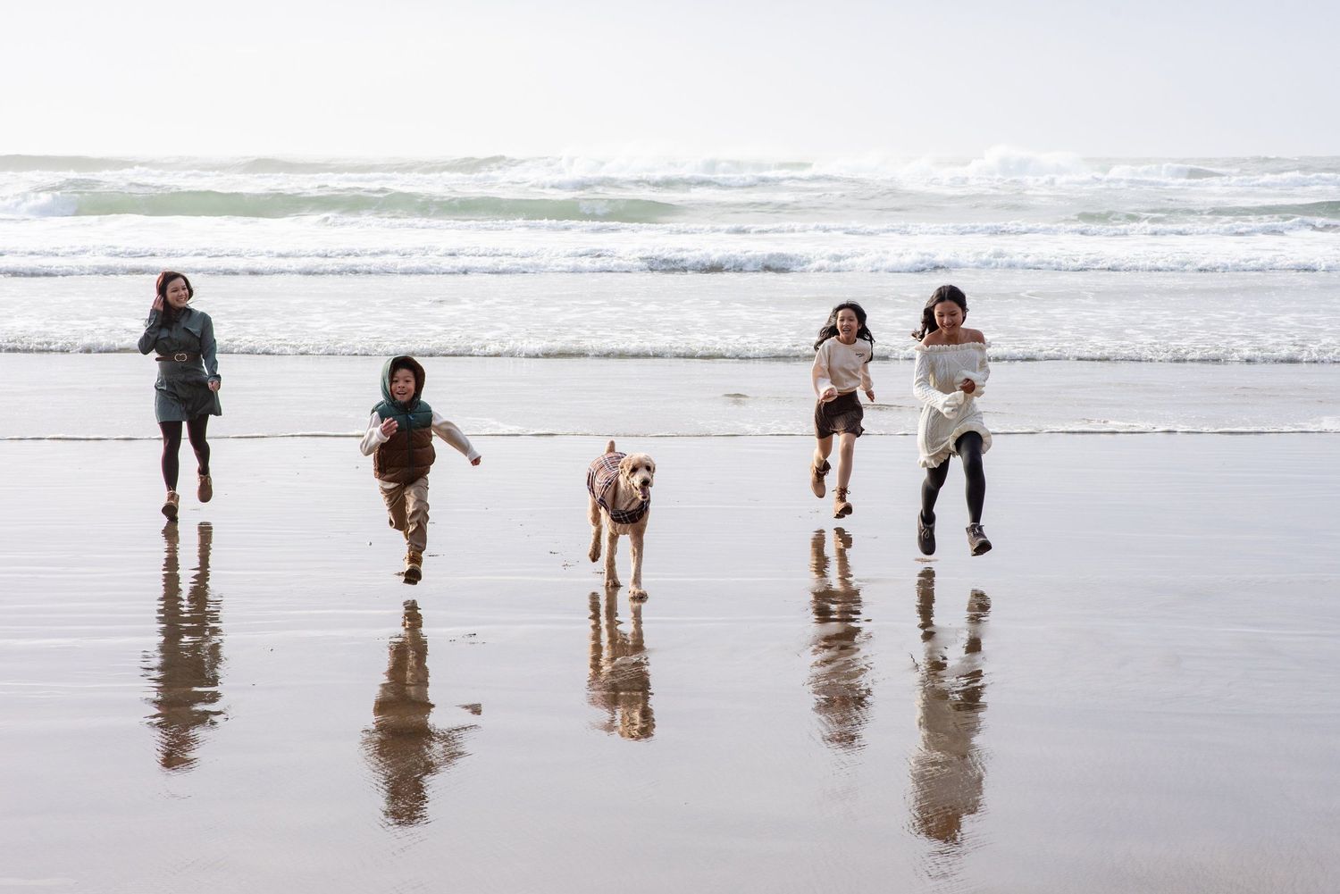 Five silhouetted figures run and play along a beach at the ocean's edge.