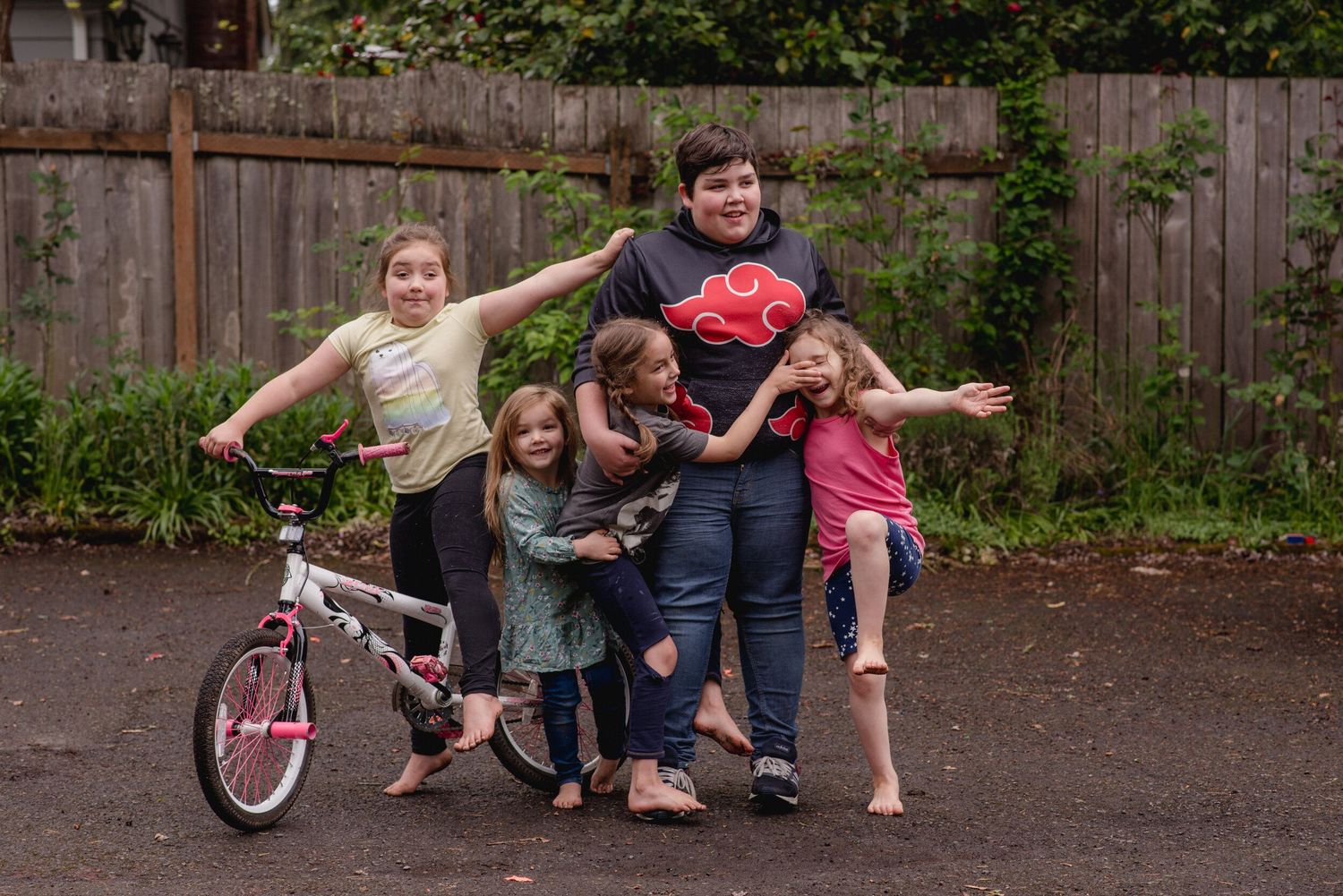 A happy group poses playfully together outdoors with a pink bicycle near a wooden fence.