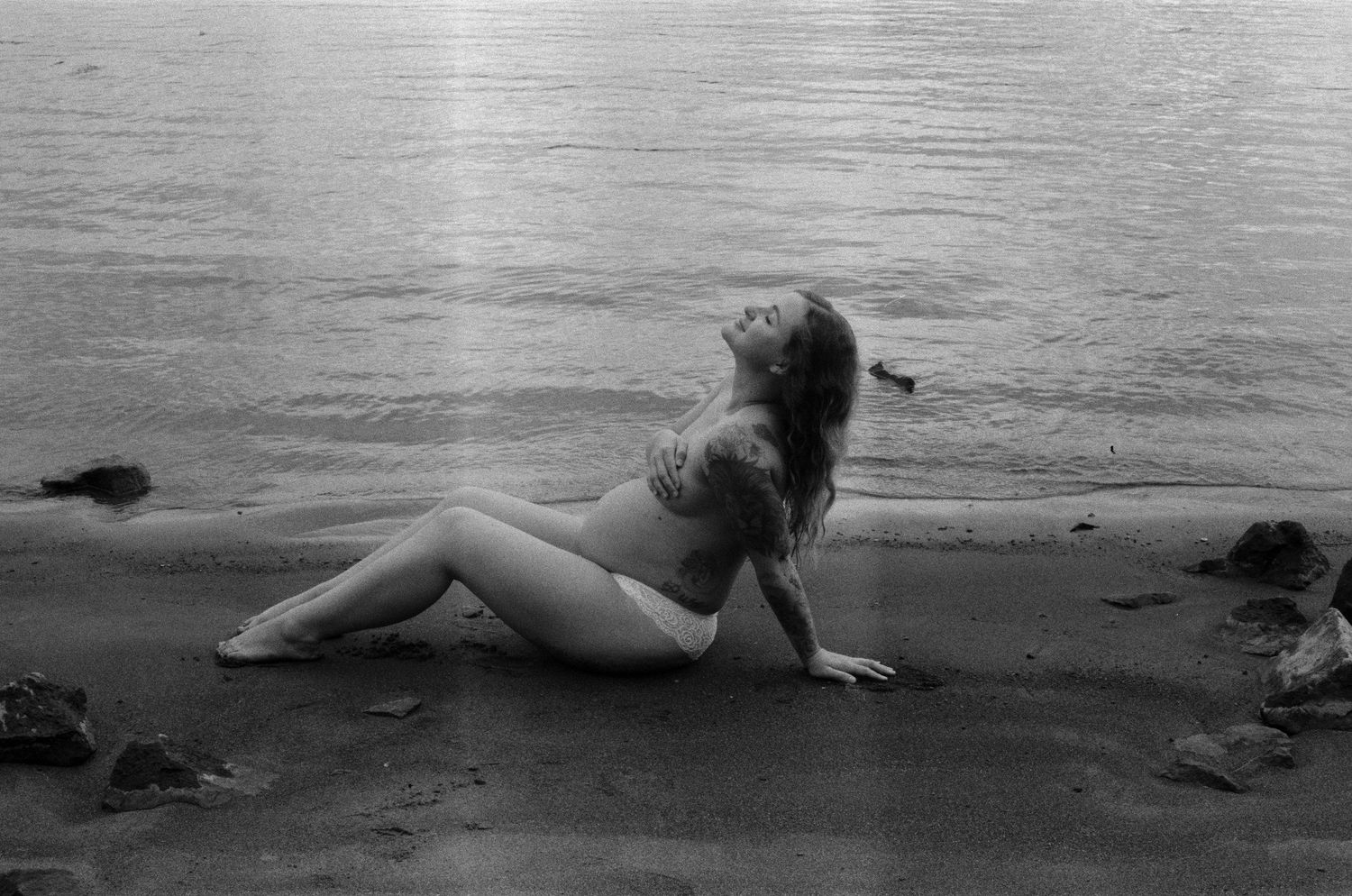 A figure reclines on dark sand at the beach in black and white.