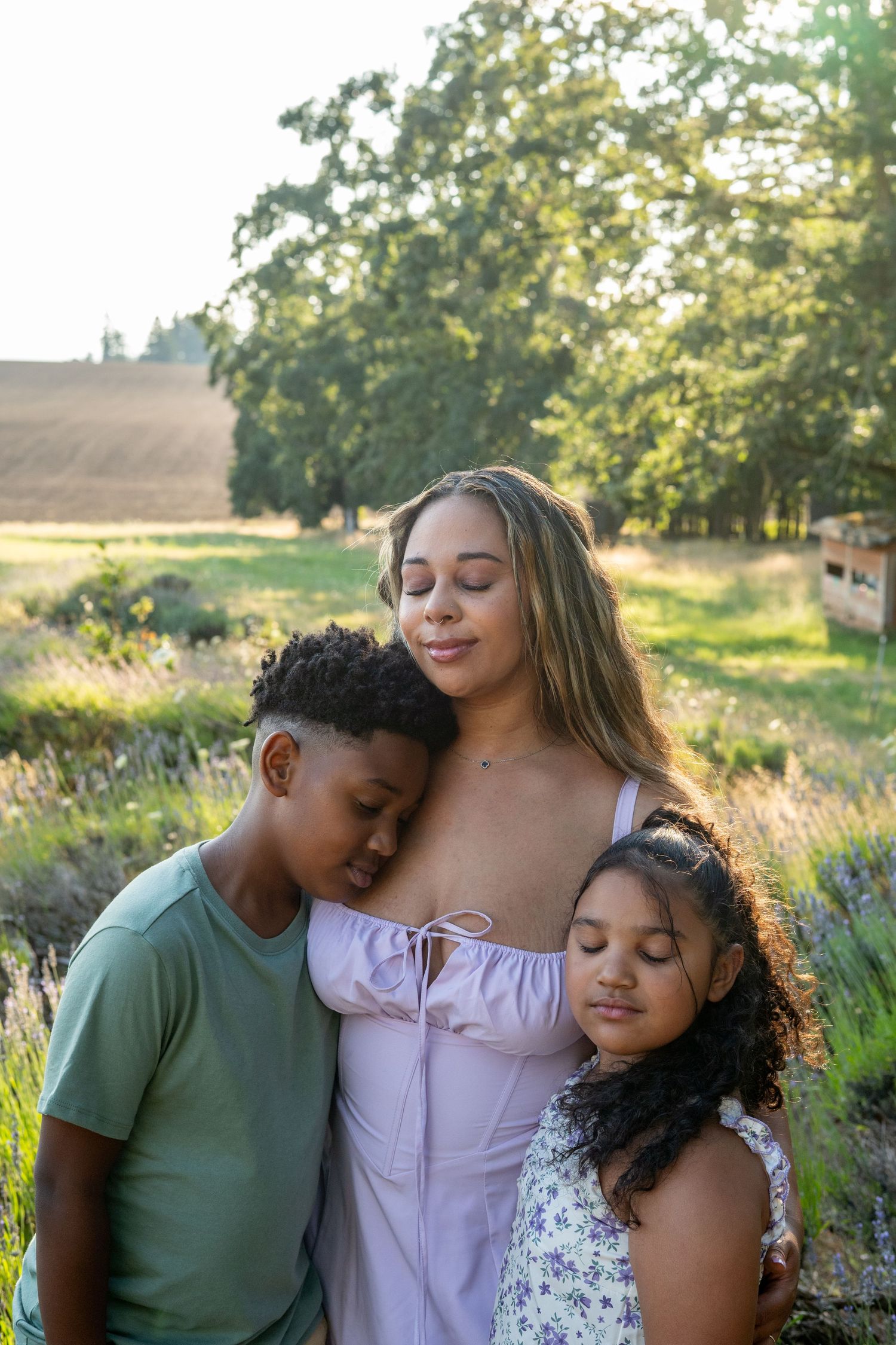 A tender moment captured in golden sunlight among lavender plants as three people embrace in a peaceful outdoor setting.
