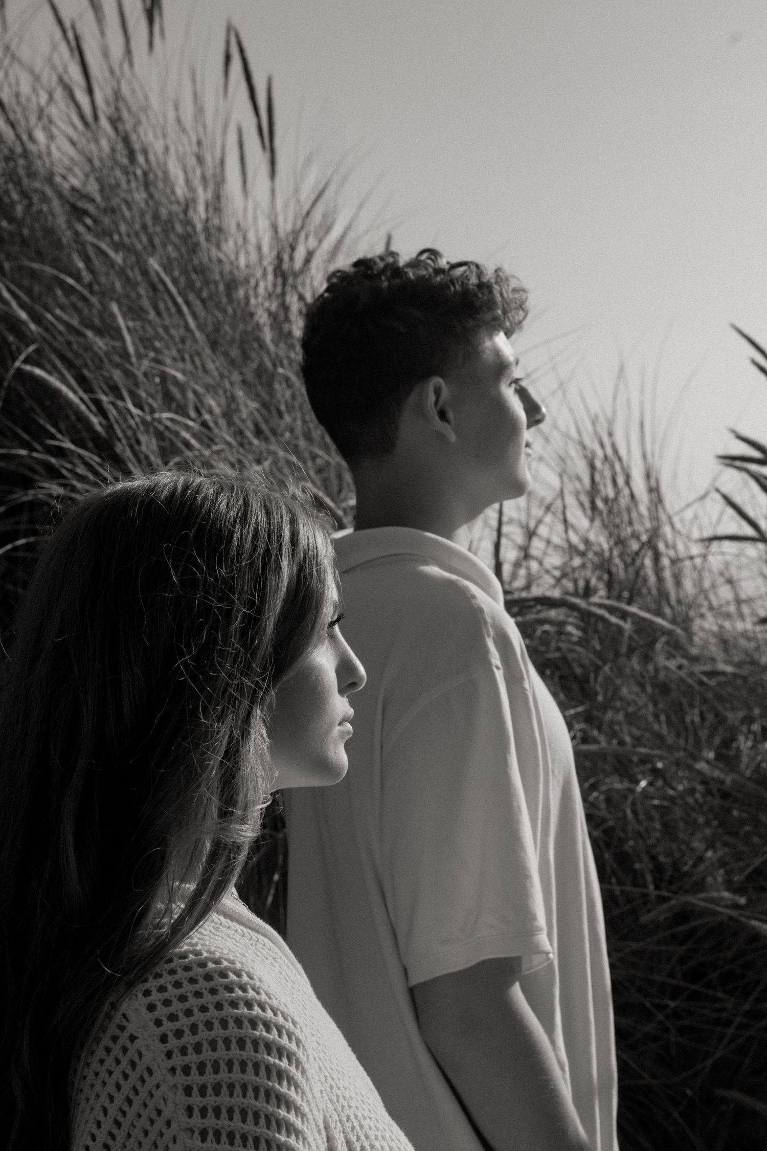 A couple standing together in tall grass shot in black and white profile view in five sequential frames.