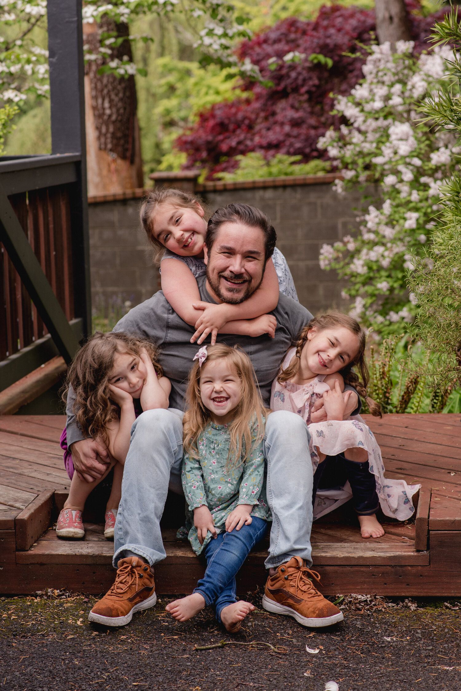 A joyful outdoor family portrait on wooden deck steps surrounded by blooming flowers.