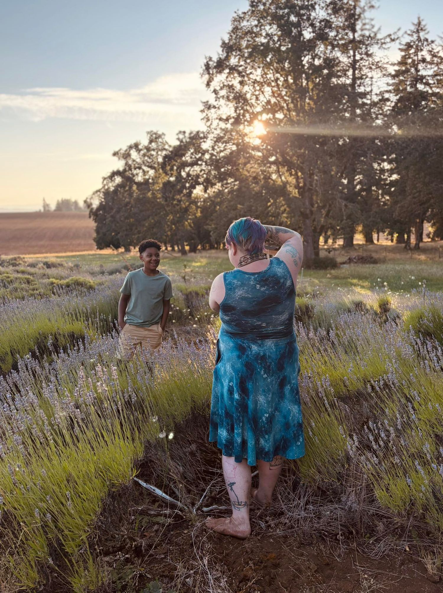 Couple embraces in a lavender field at sunset, while wearing coordinated blue outfits and standing amid purple blooms.