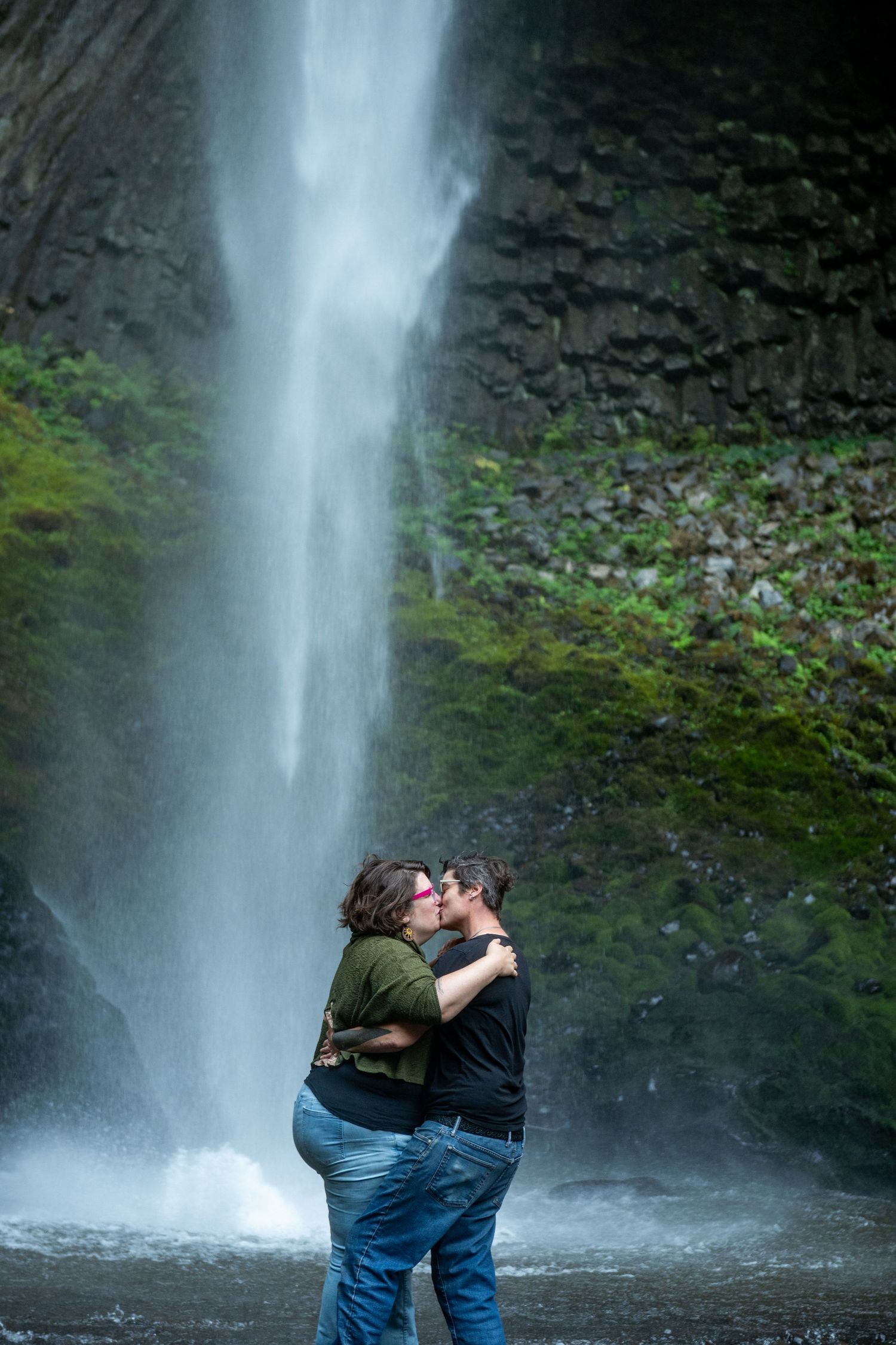 Cascading waterfall flows down mossy cliffs as a photographer captures the serene natural scene from multiple angles.