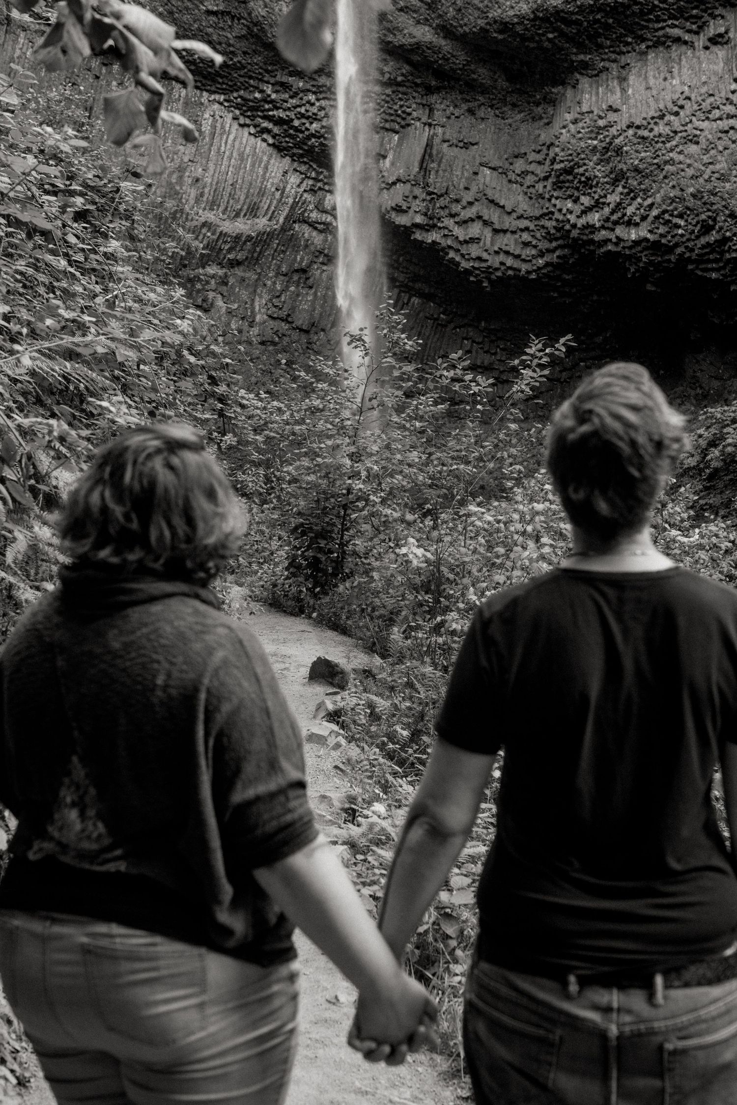 Two silhouetted figures in dark clothing sit next to each other on a rocky slope in black and white.