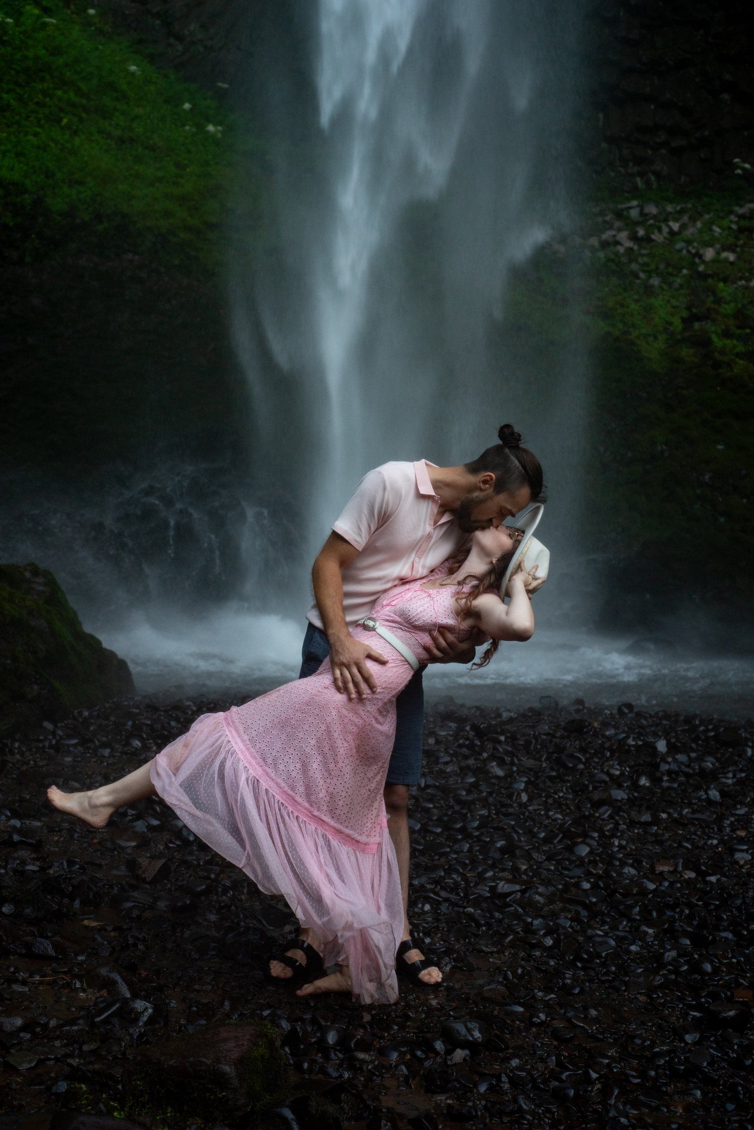 A romantic dance dip pose in front of a misty waterfall with flowing pink dress.
