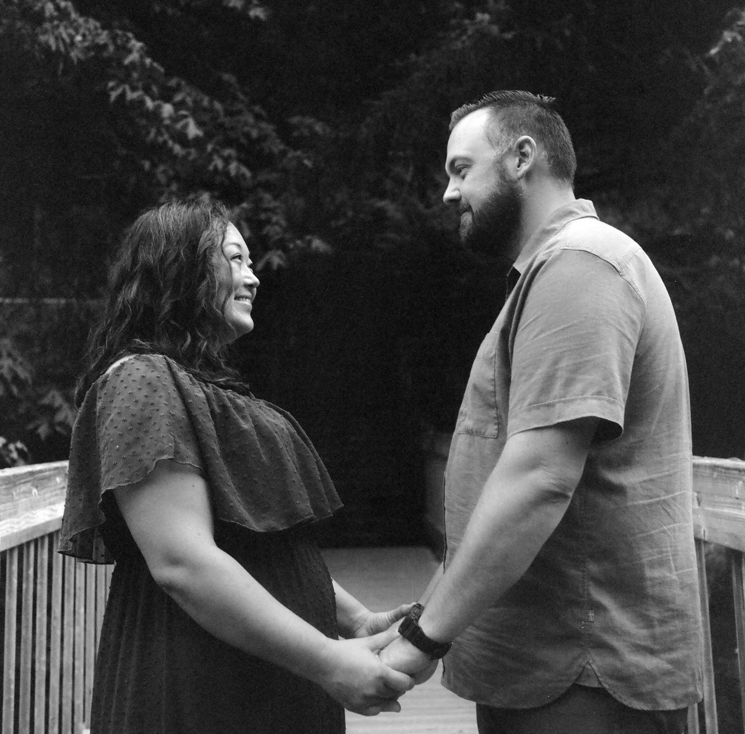 A casual outdoor engagement photo shows a couple sharing a joyful moment on a wooden deck.