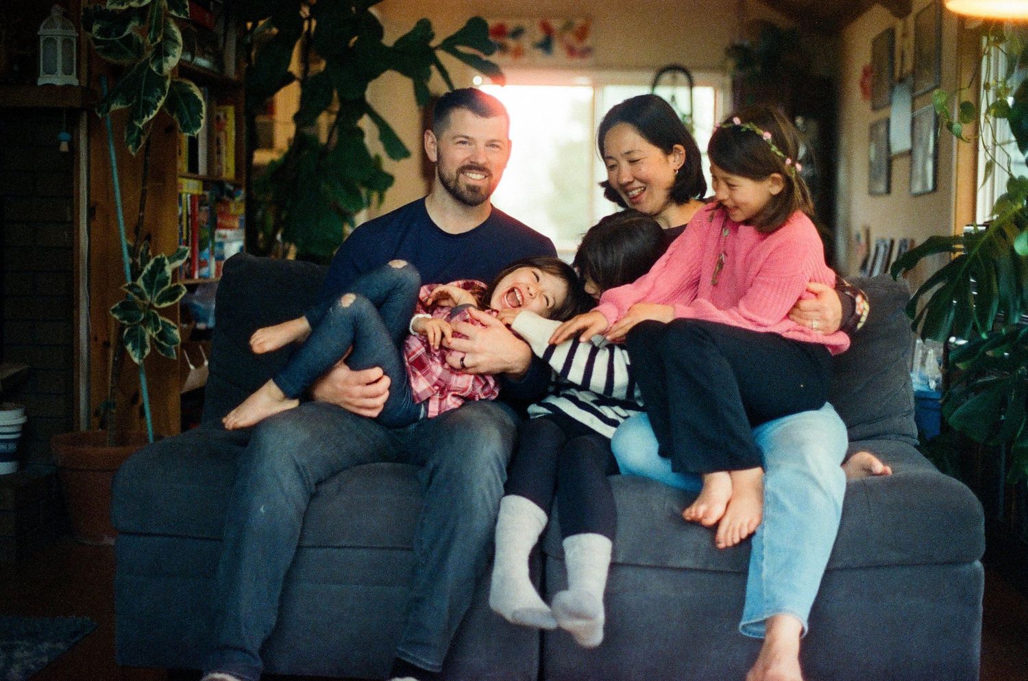 Family relaxing together on dark gray couch in living room with natural lighting.