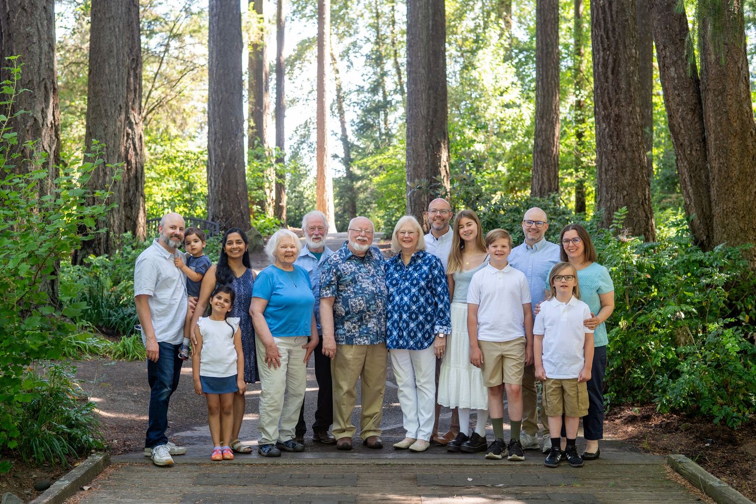 A group of people gathered outdoors among tall evergreen trees on a sunny day.