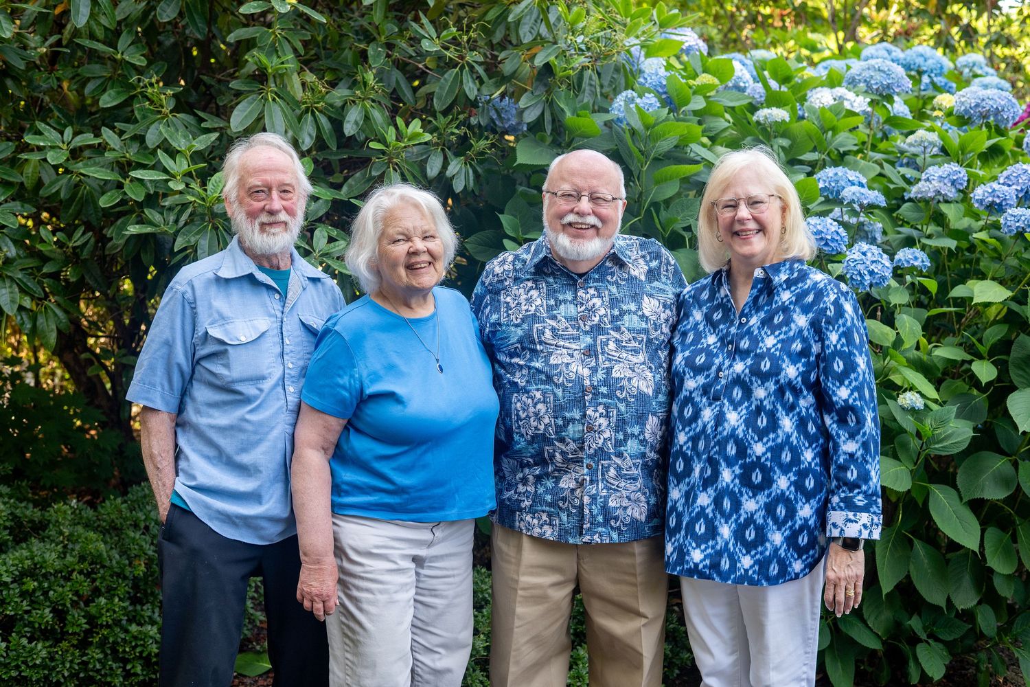 Two couples wearing coordinating blue outfits pose together in a garden setting.