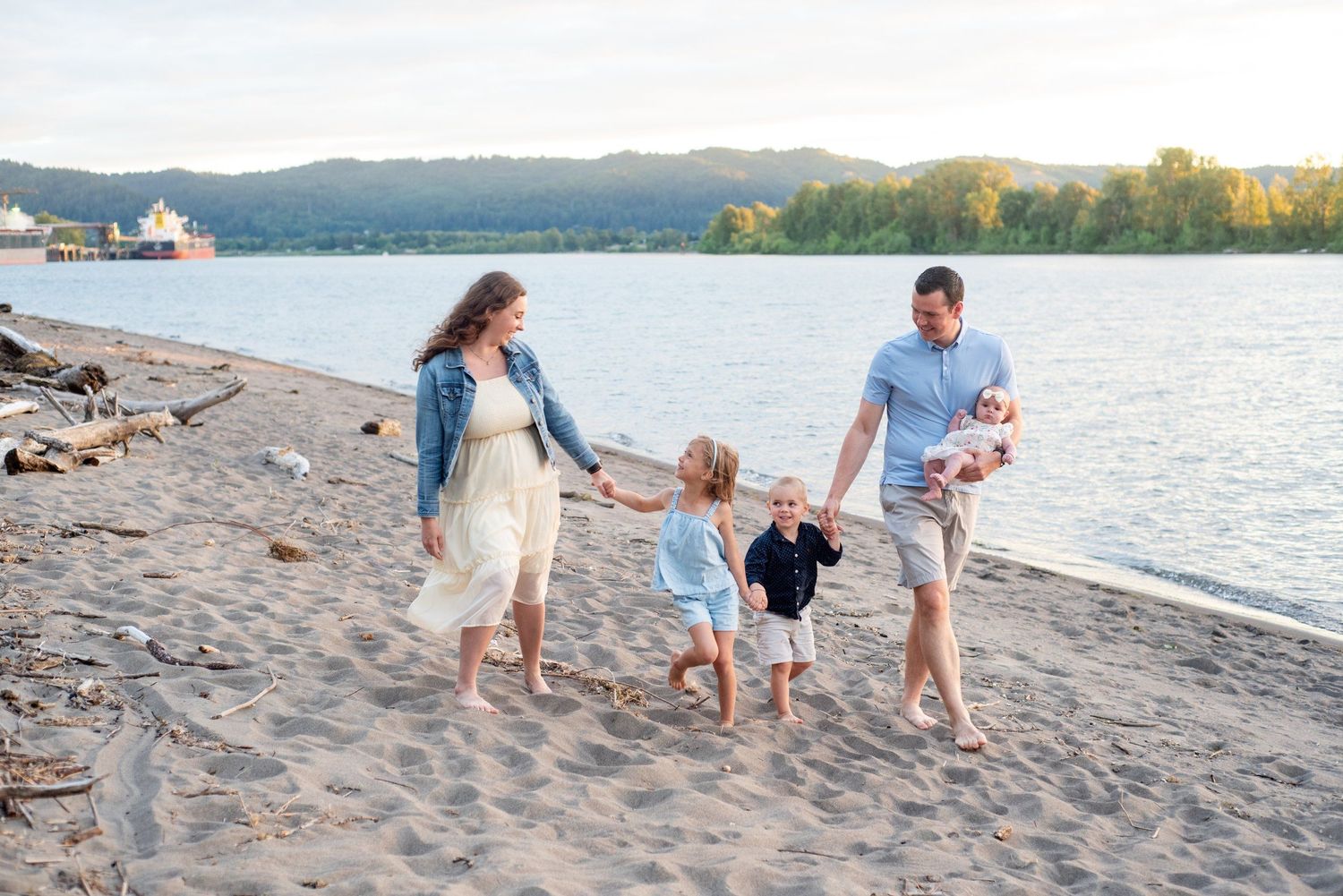 A family of five walks together along a sandy beach at sunset with mountains and water in the background.