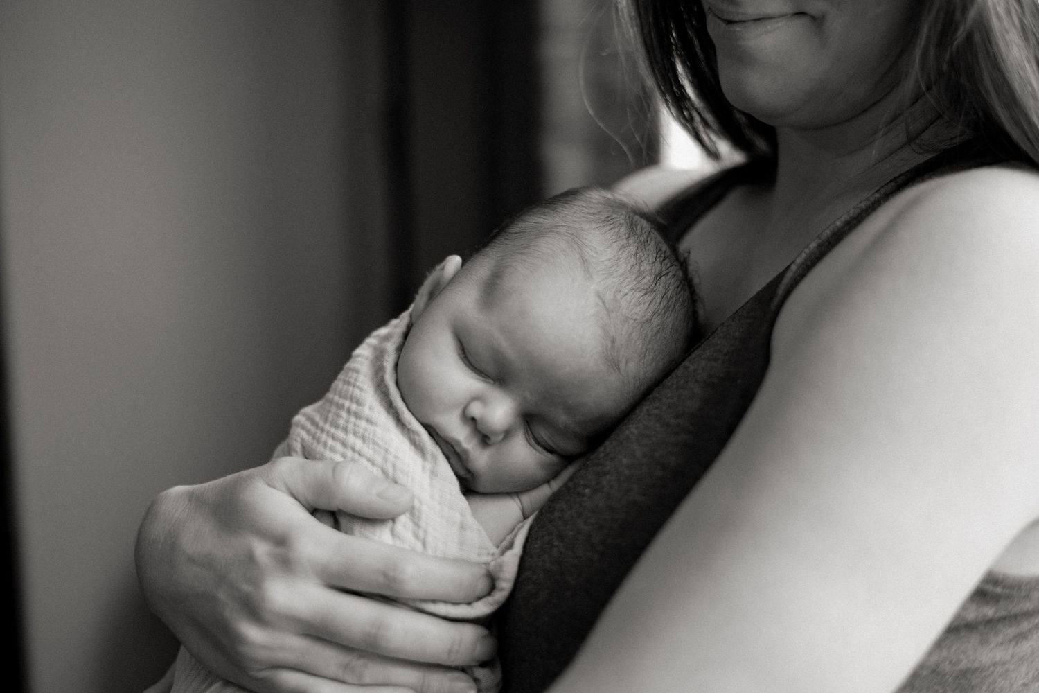 A sleeping infant rests peacefully against a mother in this intimate black and white portrait.