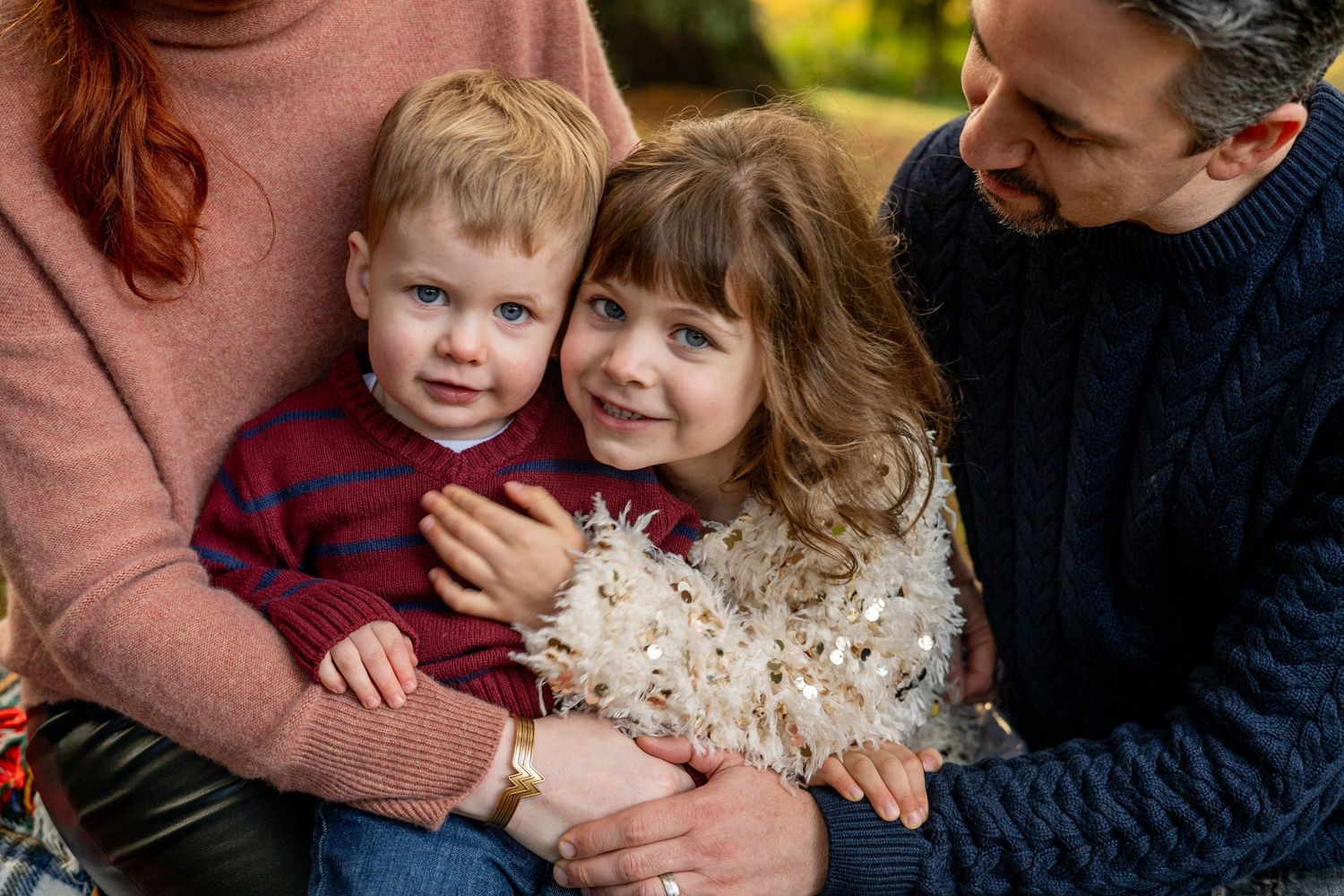 A loving family portrait with parents embracing their young children outdoors.