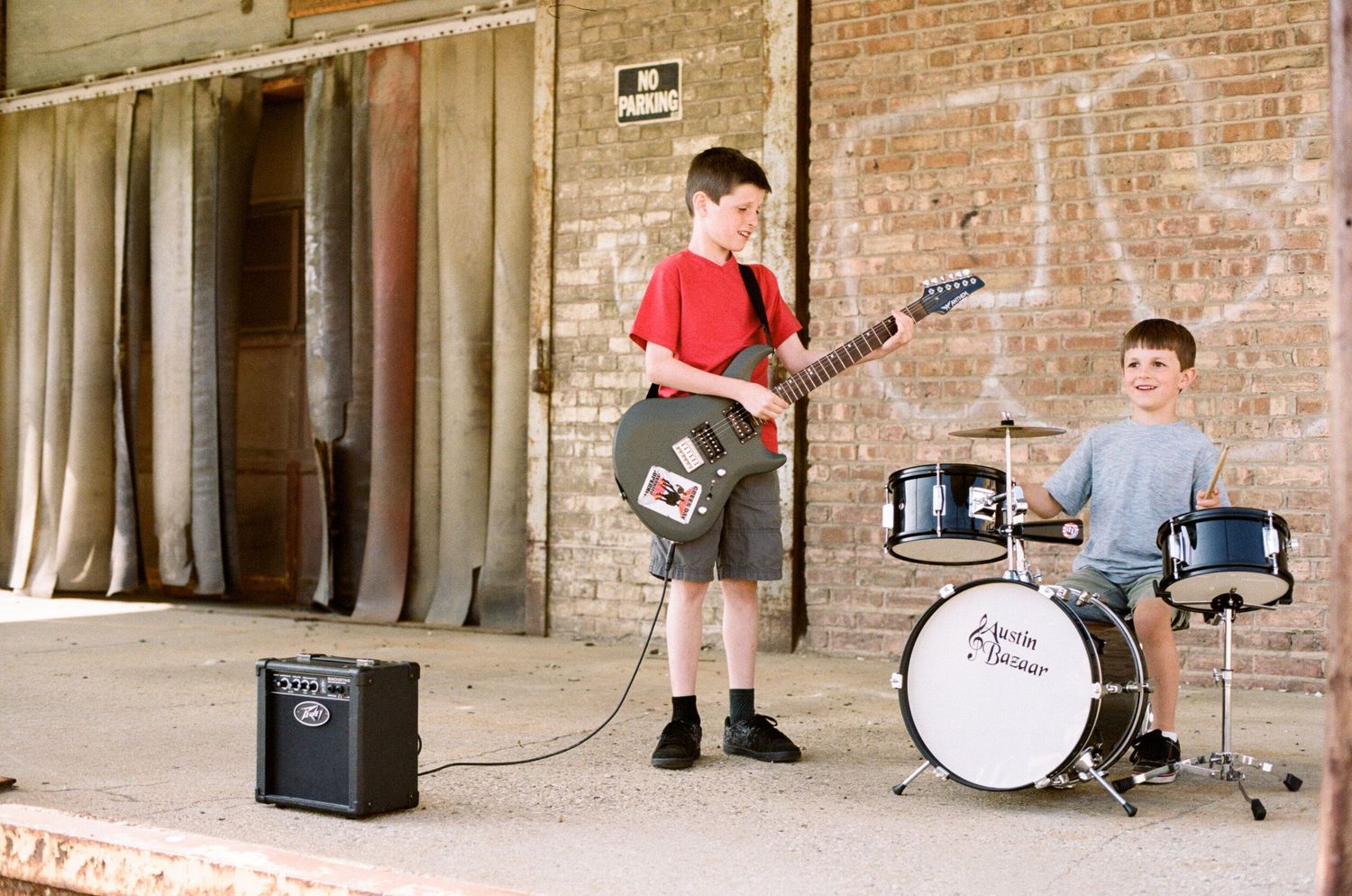 Musicians perform in front of a brick wall background in an industrial urban setting during a concert.