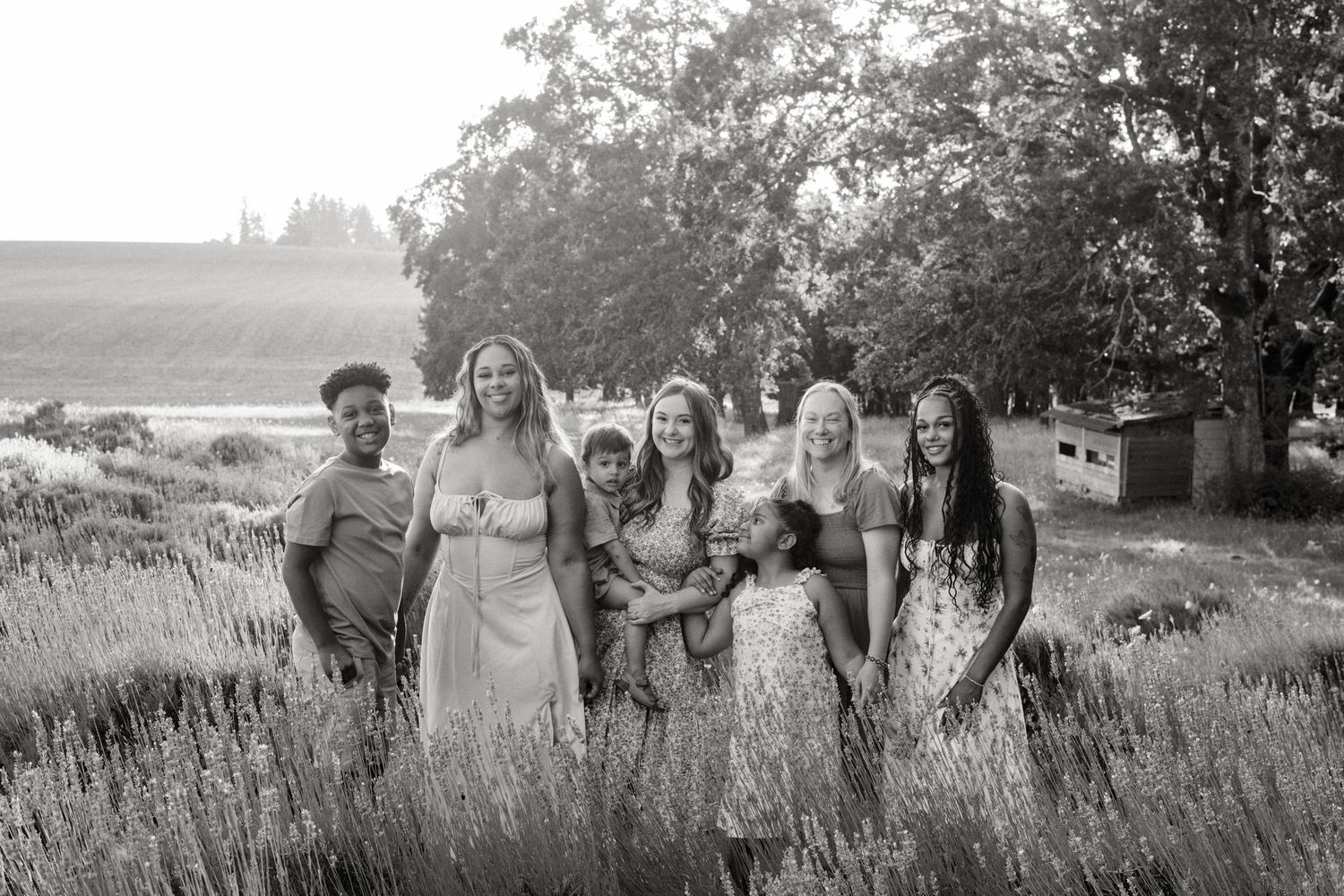 Black and white portrait of a bridal party standing together in a rustic field with tall grass and trees in the background.