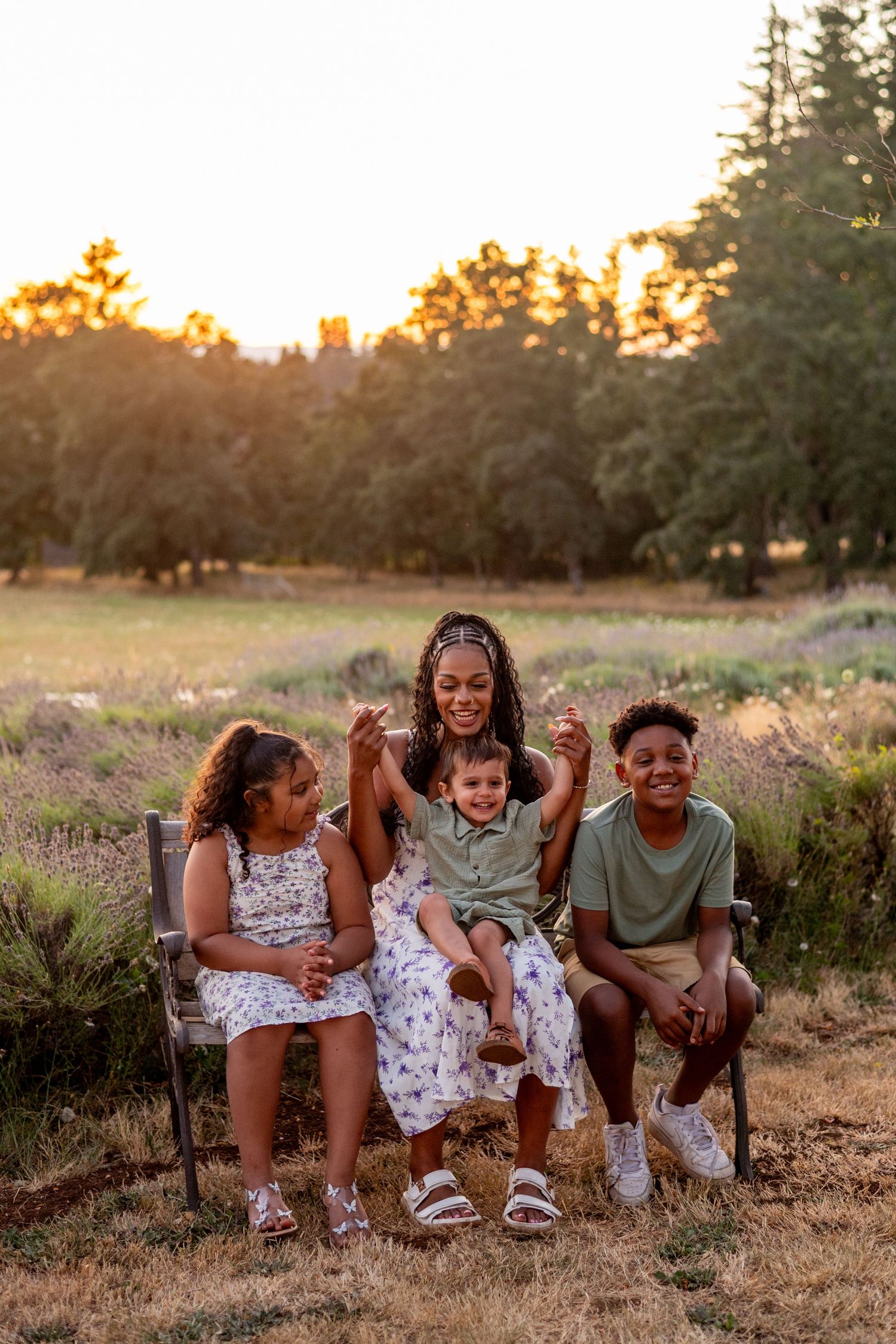 A group sits together laughing outdoors in a field at sunset with lavender plants and evergreen trees in background.